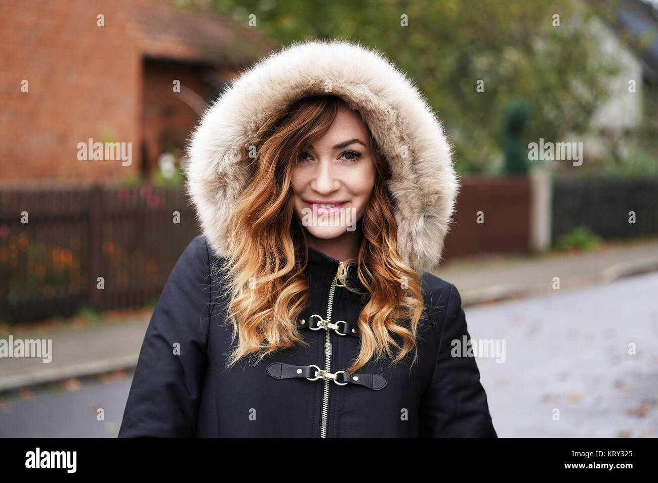 Sorridente giovane donna indossa cappotto invernale con pelliccia finta il cofano Foto Stock