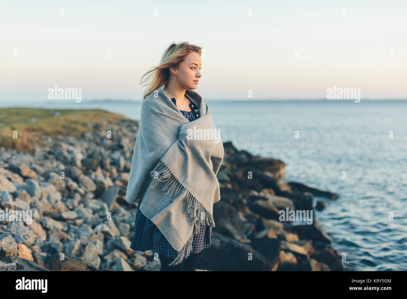 Una giovane donna avvolta in uno scialle che guarda al mare Foto stock -  Alamy