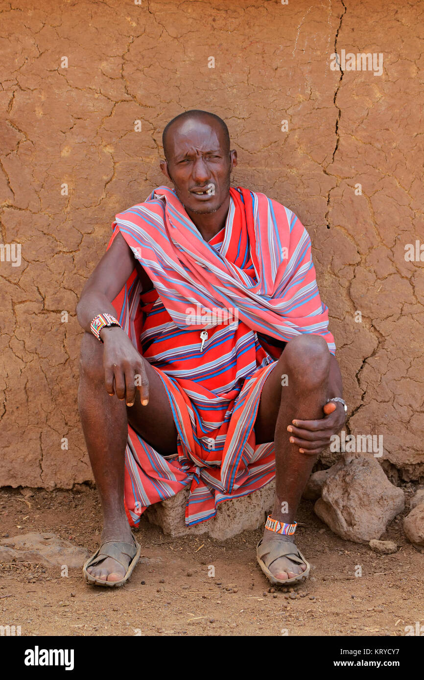 AMBOSELI, KENYA - Agosto 31, 2013:Non identificato uomo Masai con tradizionale indumento colorato seduto davanti alla sua capanna, Amboseli, Kenya Foto Stock