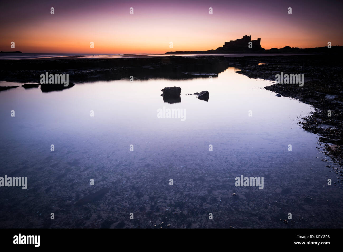 Il castello di Bamburgh in Northumberland si vede attraverso rockpools all'alba Foto Stock