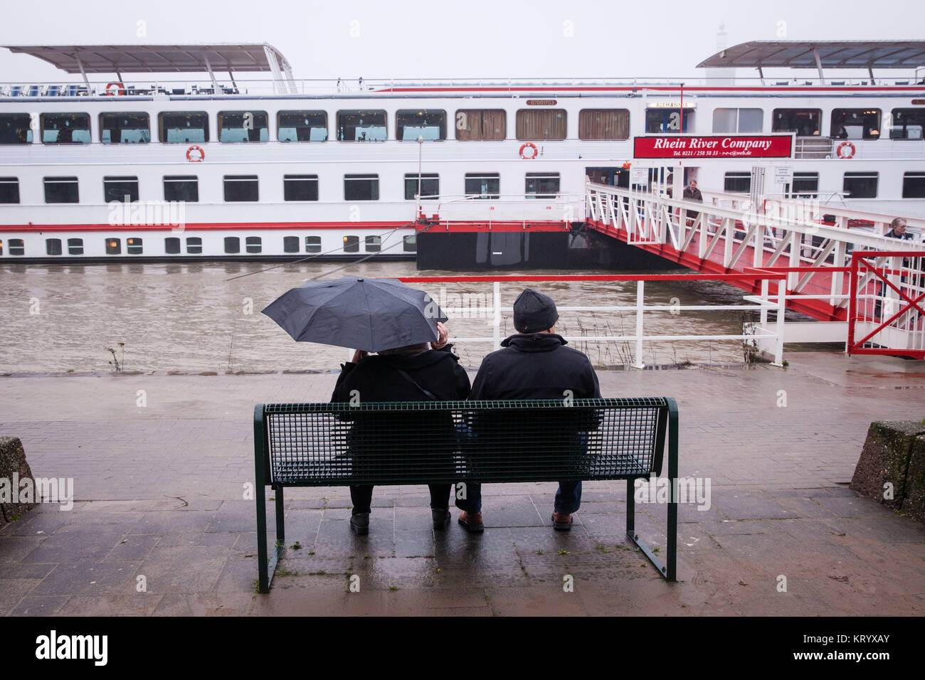 L'Europa, Germania, Colonia, in un giorno di pioggia una coppia di anziani seduti su una panchina sulle rive del fiume Reno, luce di allagamento. Europa, Deutschland, Koe Foto Stock