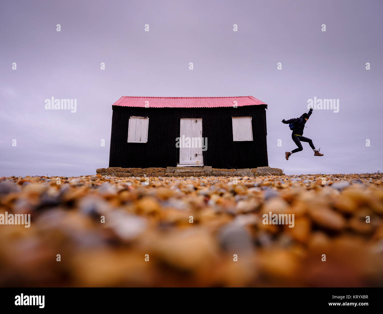 Una donna salta dal lato di un piccolo nero e rosso rifugio sulla riva del fiume in Rye Harbour Riserva Naturale, East Sussex Regno Unito Foto Stock