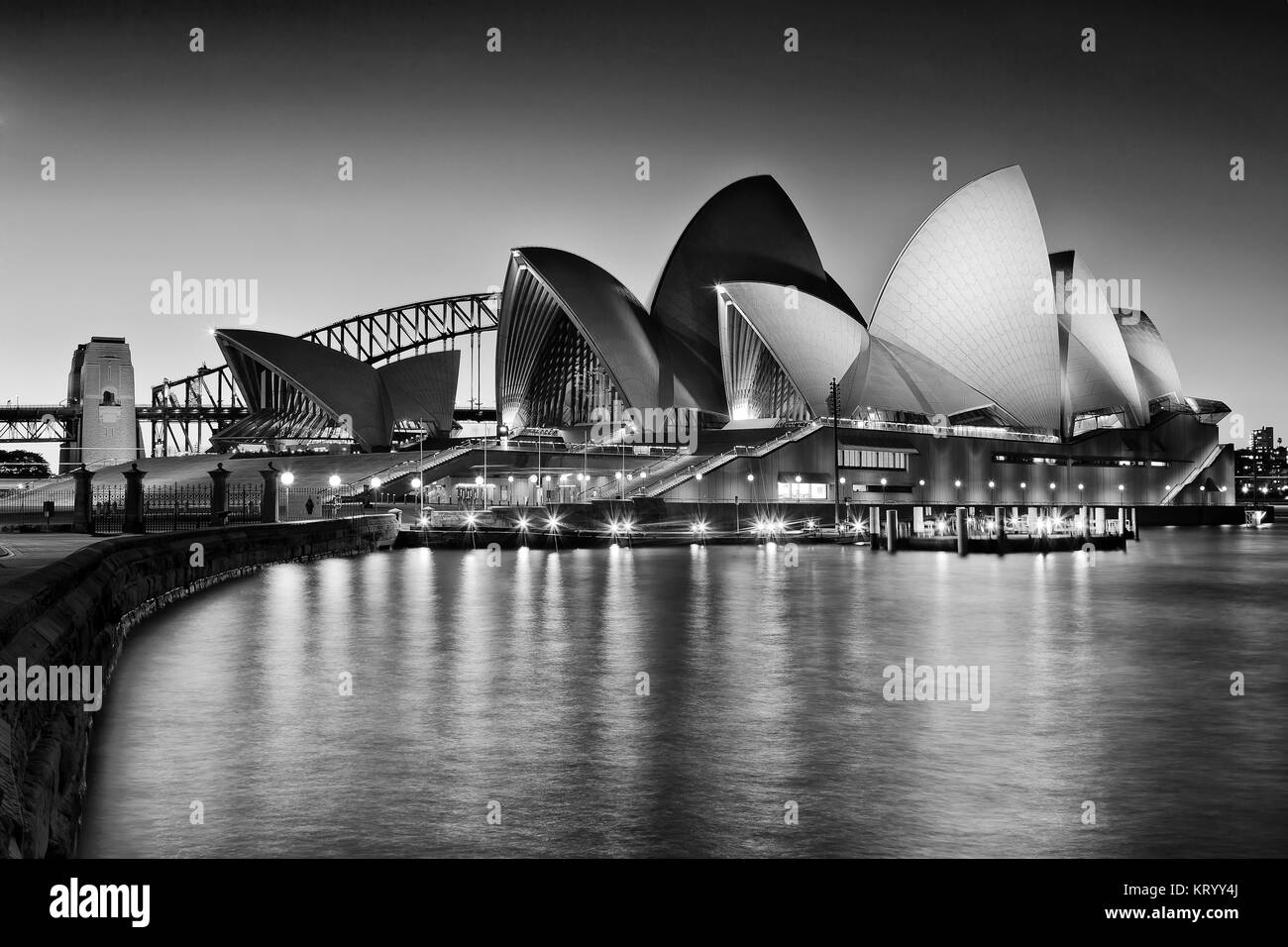 SYDNEY, AUSTRALIA, 1 luglio 2016 - Sydney Opera House e Harbour Bridge al tramonto che riflettono le luci di illuminazione in sfocato cove acque come visto da R Foto Stock