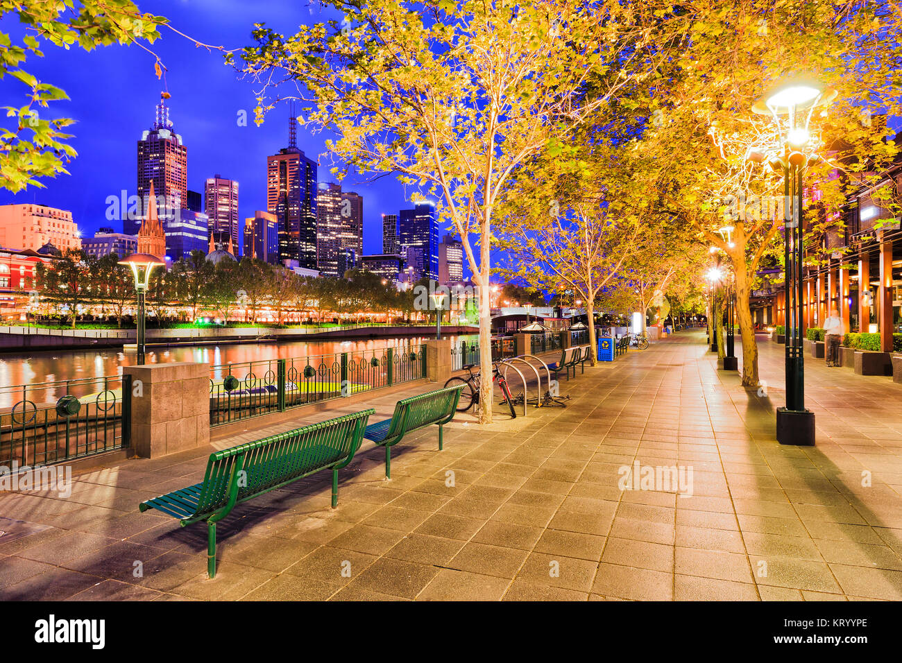 Il Boardwalk per gli acquirenti di Southbank sul fiume Yarra lato nella città di Melbourne CBD di sunrise sotto alberi frondosi e illuminato lampade stradali. Foto Stock