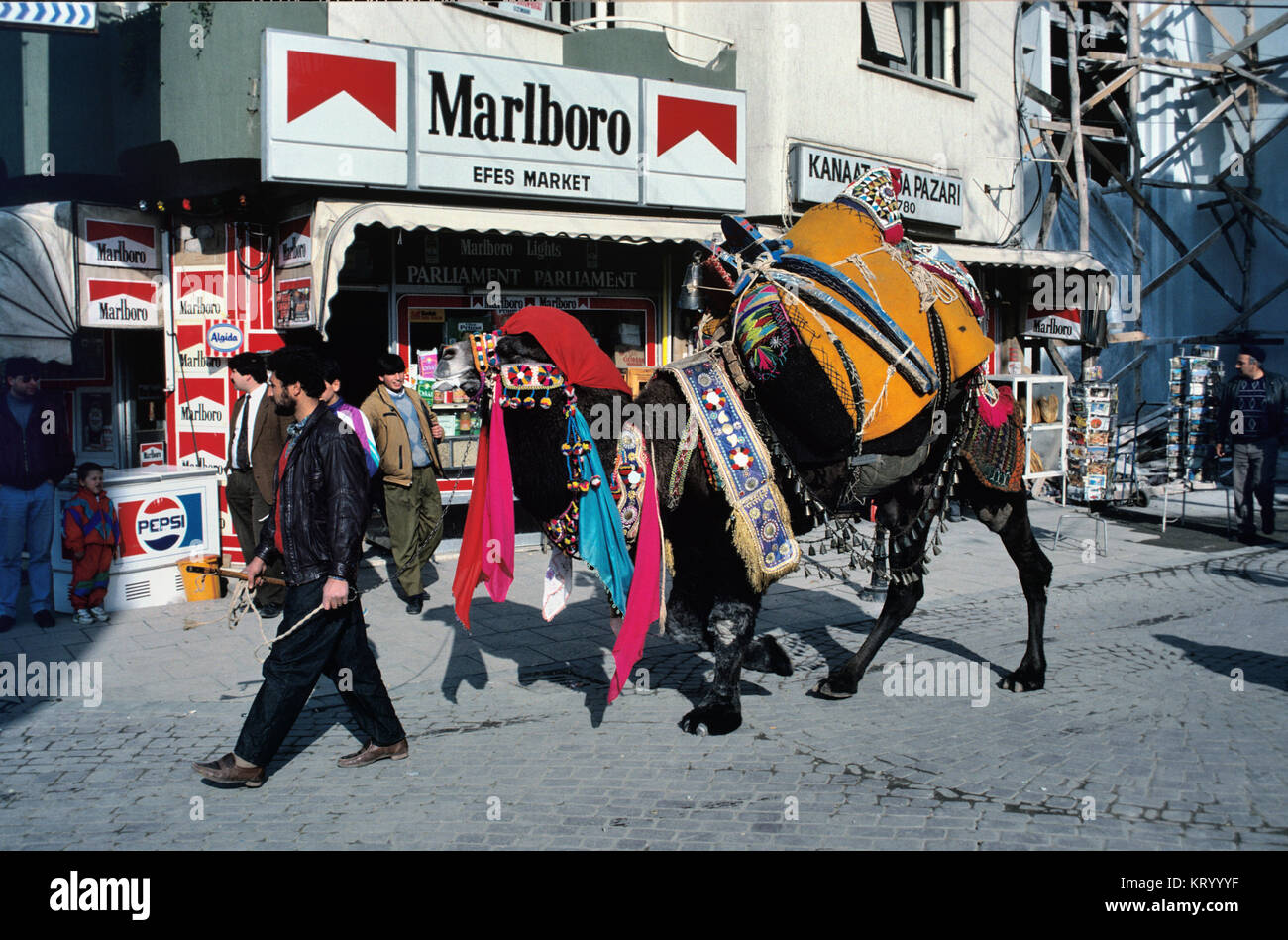 Uomo con vestito Camel o Wrestling Camel camminando per strada di fronte a magazzino generale, Convenience Store o Corner Shop in Selçuk, regione del Mar Egeo, Turchia Foto Stock