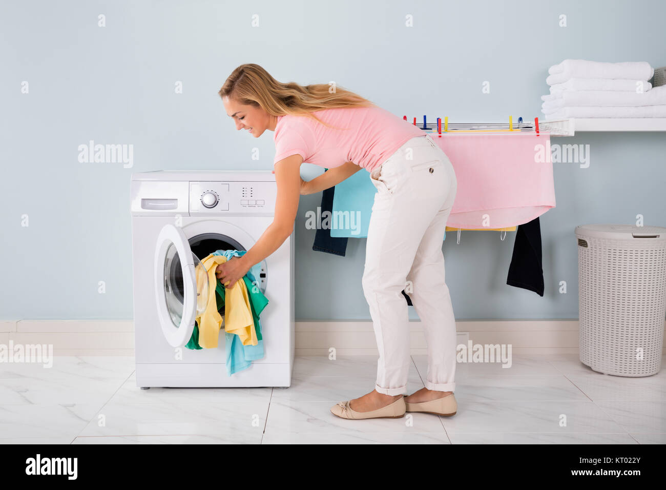 Donna sorridente mettendo i vestiti nella macchina di lavaggio Foto Stock