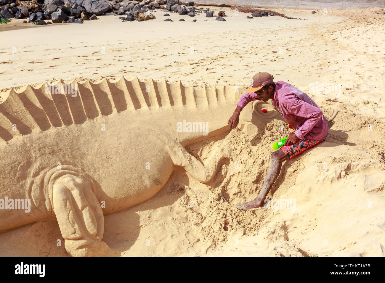 Uomo locale per scolpire un camaleonte dalla sabbia sulla spiaggia di Santa Maria, Isola di Sal, Salina, Capo Verde, Africa Foto Stock