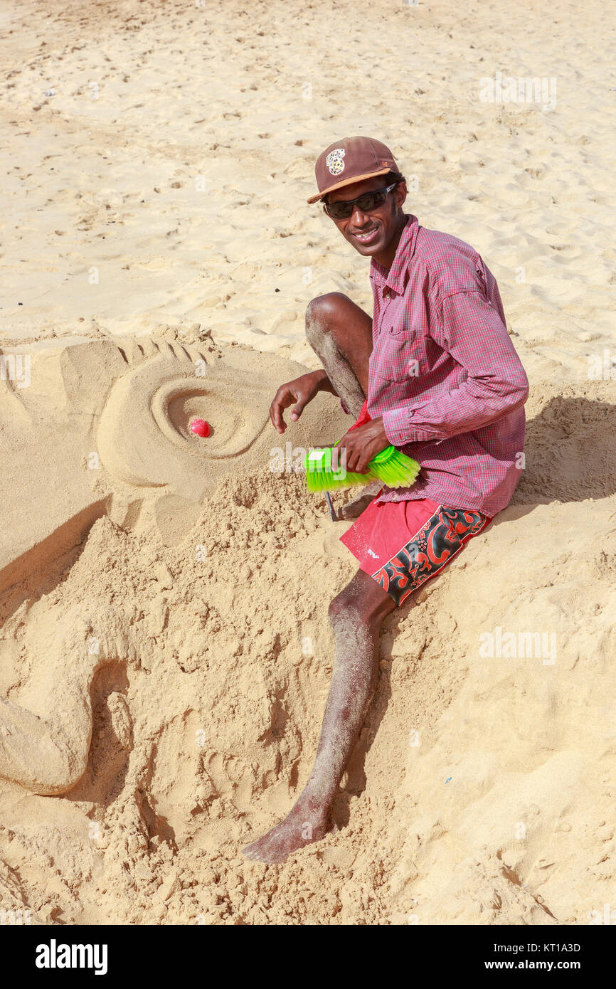 Uomo locale per scolpire un camaleonte o lizard ritratto nella sabbia sulla spiaggia di Santa Maria, Isola di Sal, Salina, Capo Verde, Africa Foto Stock