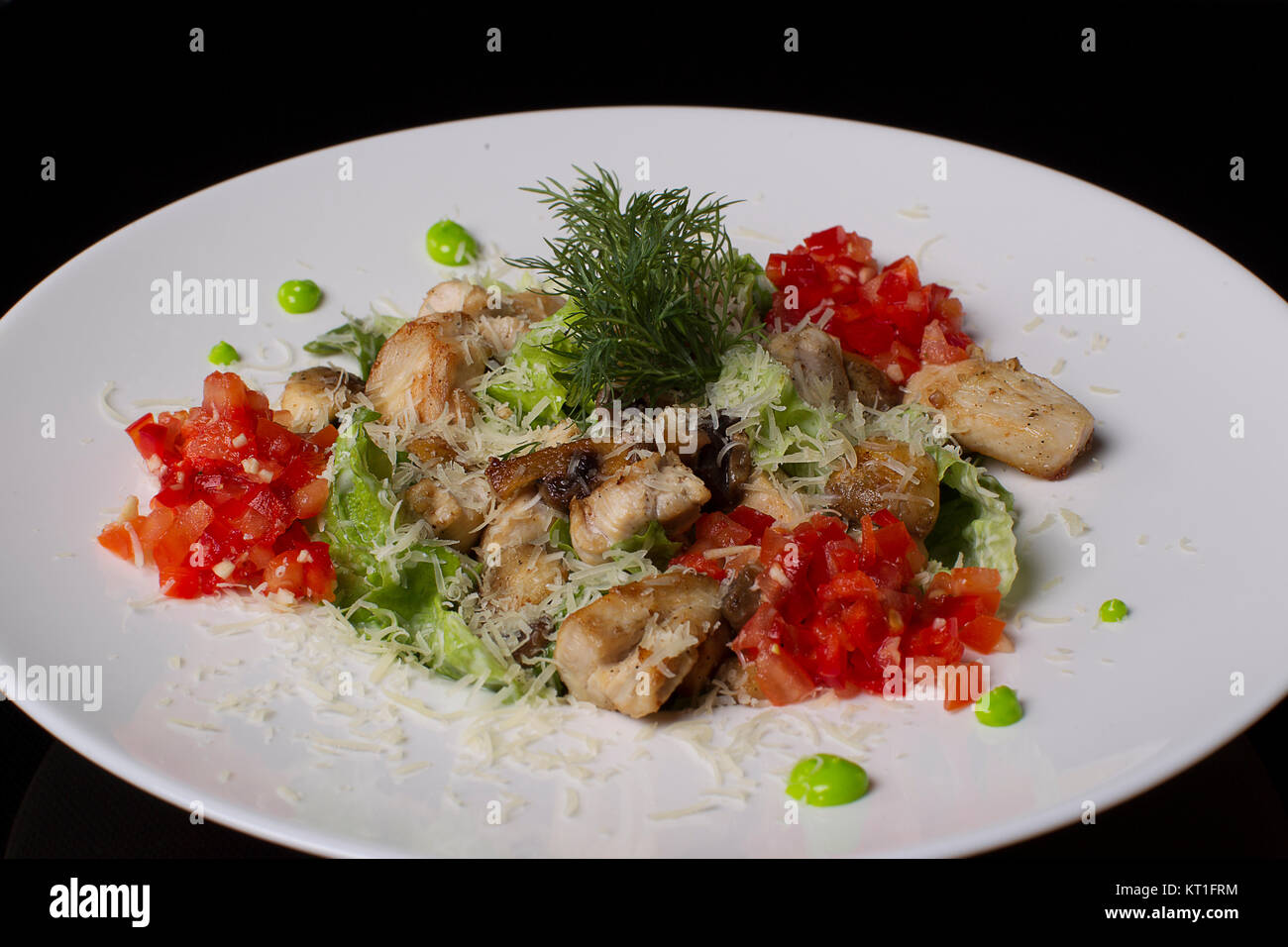 Su una piastra bianca Insalata di carne, pomodori, lattuga, aneto, cosparso con formaggio, su uno sfondo nero.la carne fritta con verdure. Foto Stock