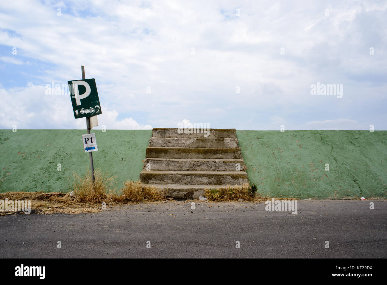 Strada laterale di un vecchio colorato terrapieno verde con una scala e un simbolo di parcheggio con uno sfondo con cielo nuvoloso Foto Stock