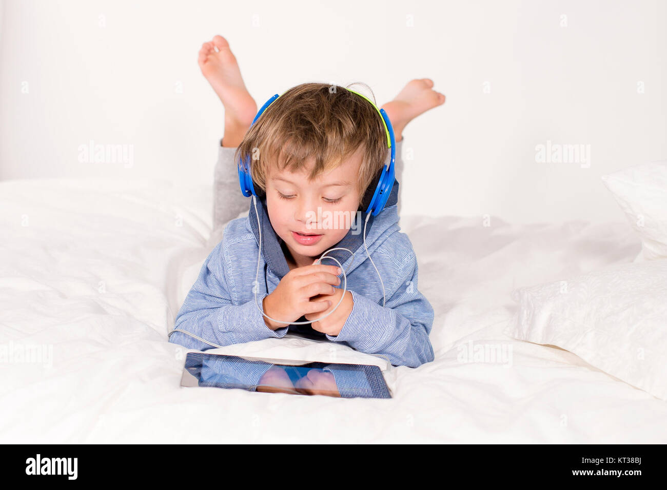 Ein Junge liegt mit Notebook und Kopfhörer auf einem Bett Foto Stock