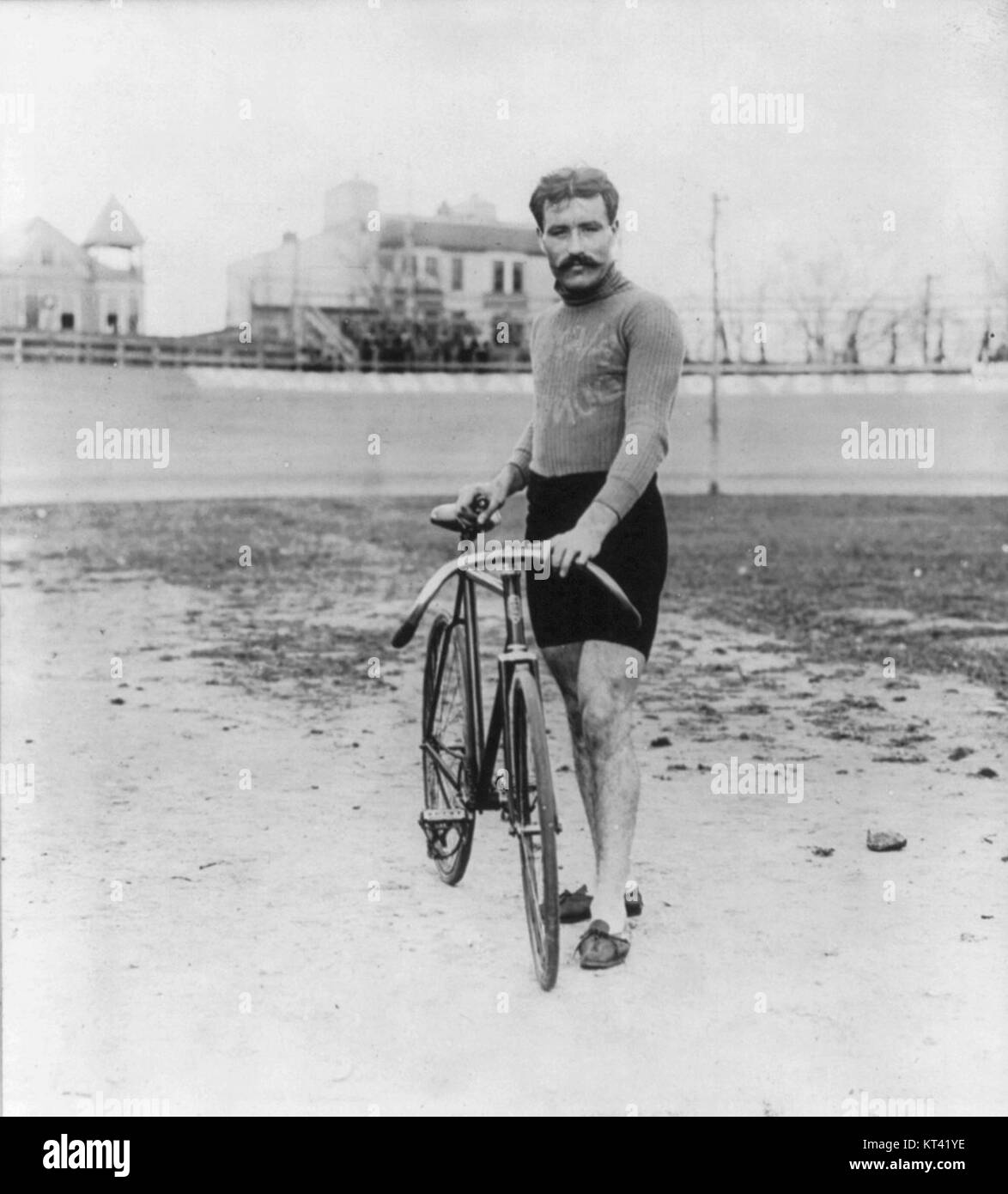 Un ritratto a figura intera di Léon Georget, in piedi e rivolto in avanti, tenendo in mano una bicicletta. L'immagine cattura la sua postura e il suo abbigliamento, dando uno sguardo alla moda e alle pratiche sociali del tempo, con particolare attenzione alla bicicletta come simbolo iconico della mobilità durante l'epoca. Foto Stock