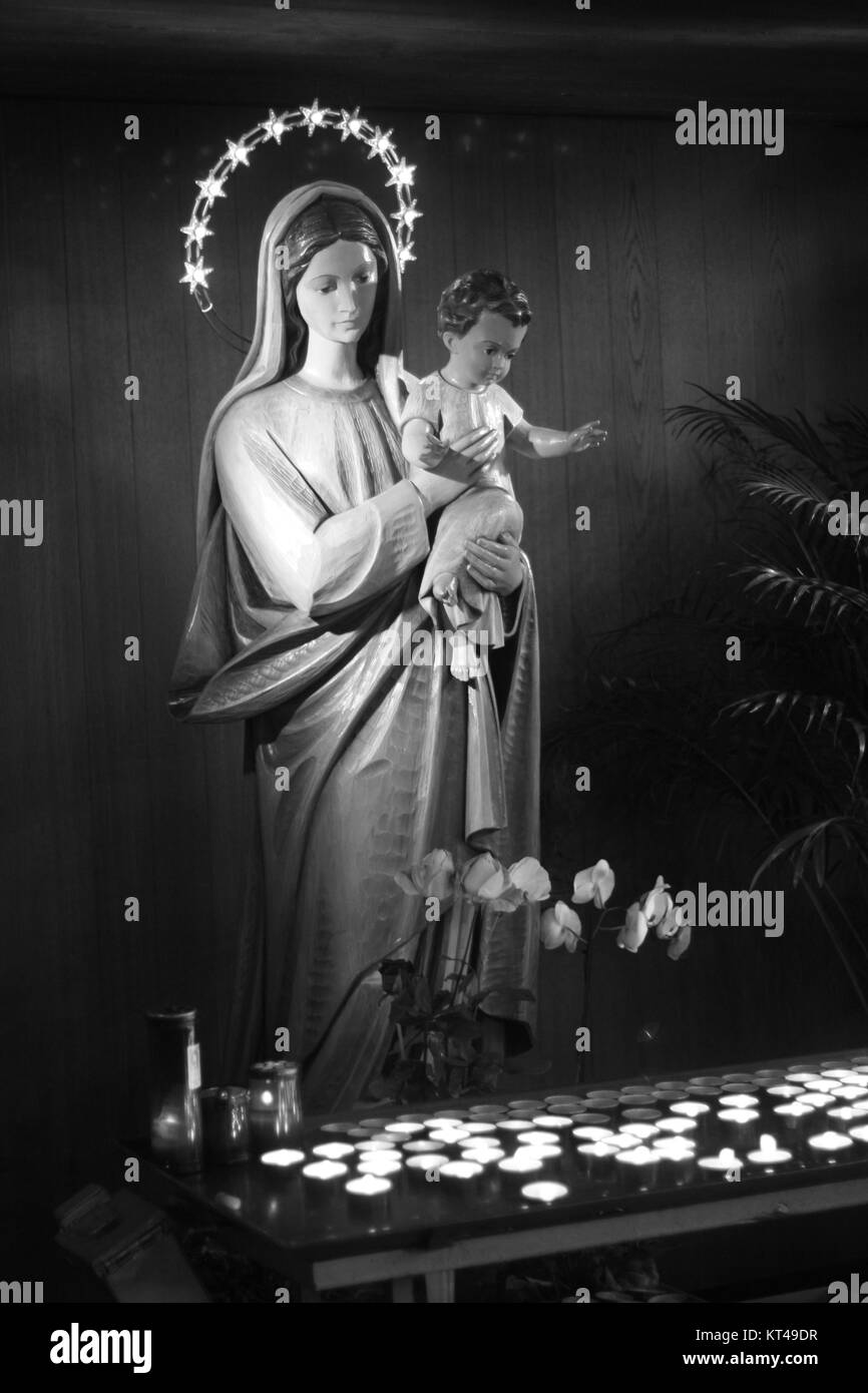 Maria e Gesù bambino statua con candele votive. La religione icona cattolica. In bianco e nero. Foto Stock