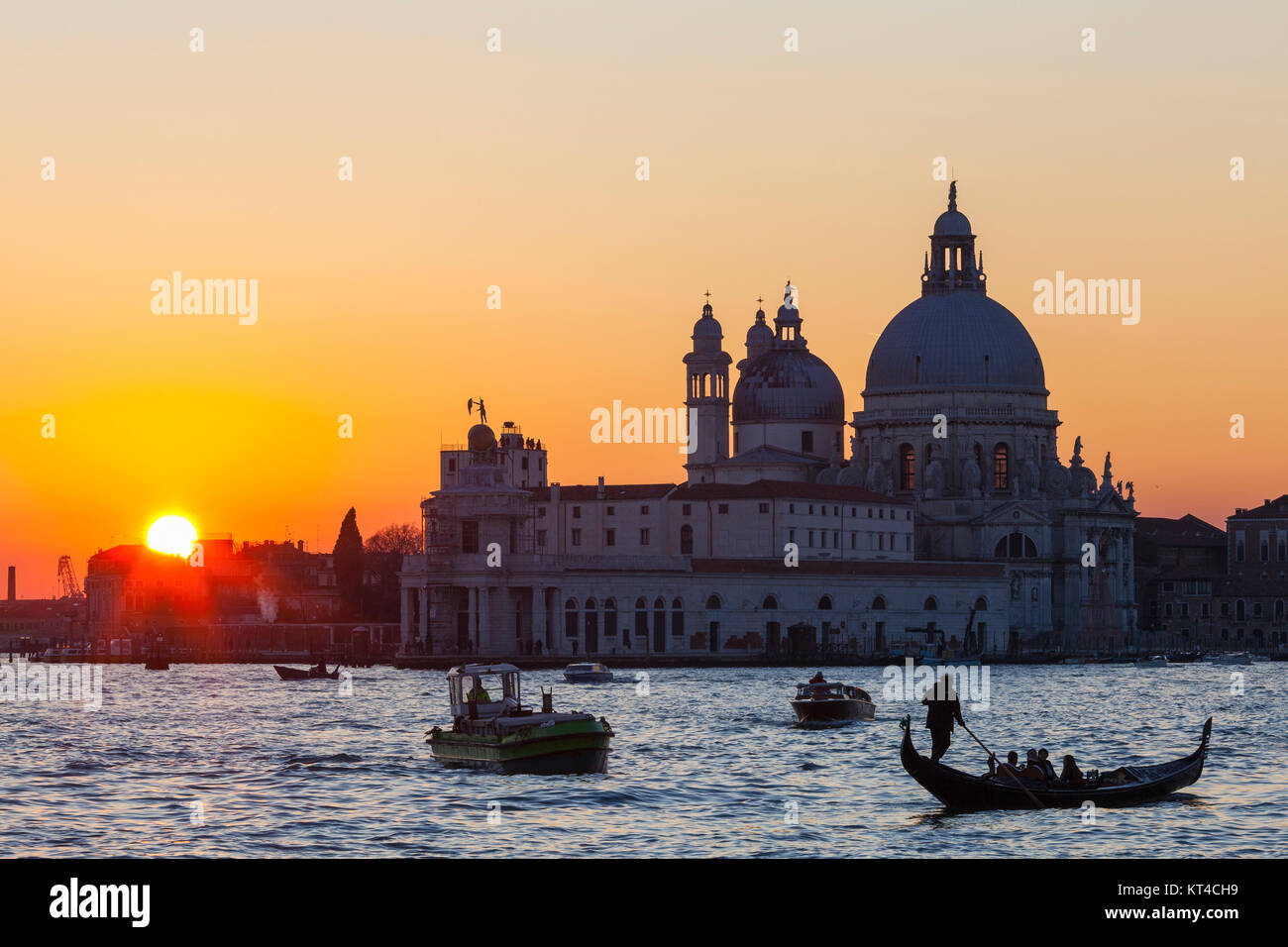Colorato arancione tramonto sulla laguna di Venezia e la Basilica di Santa Maria della Salute con barche e una gondola con i turisti in primo piano Foto Stock