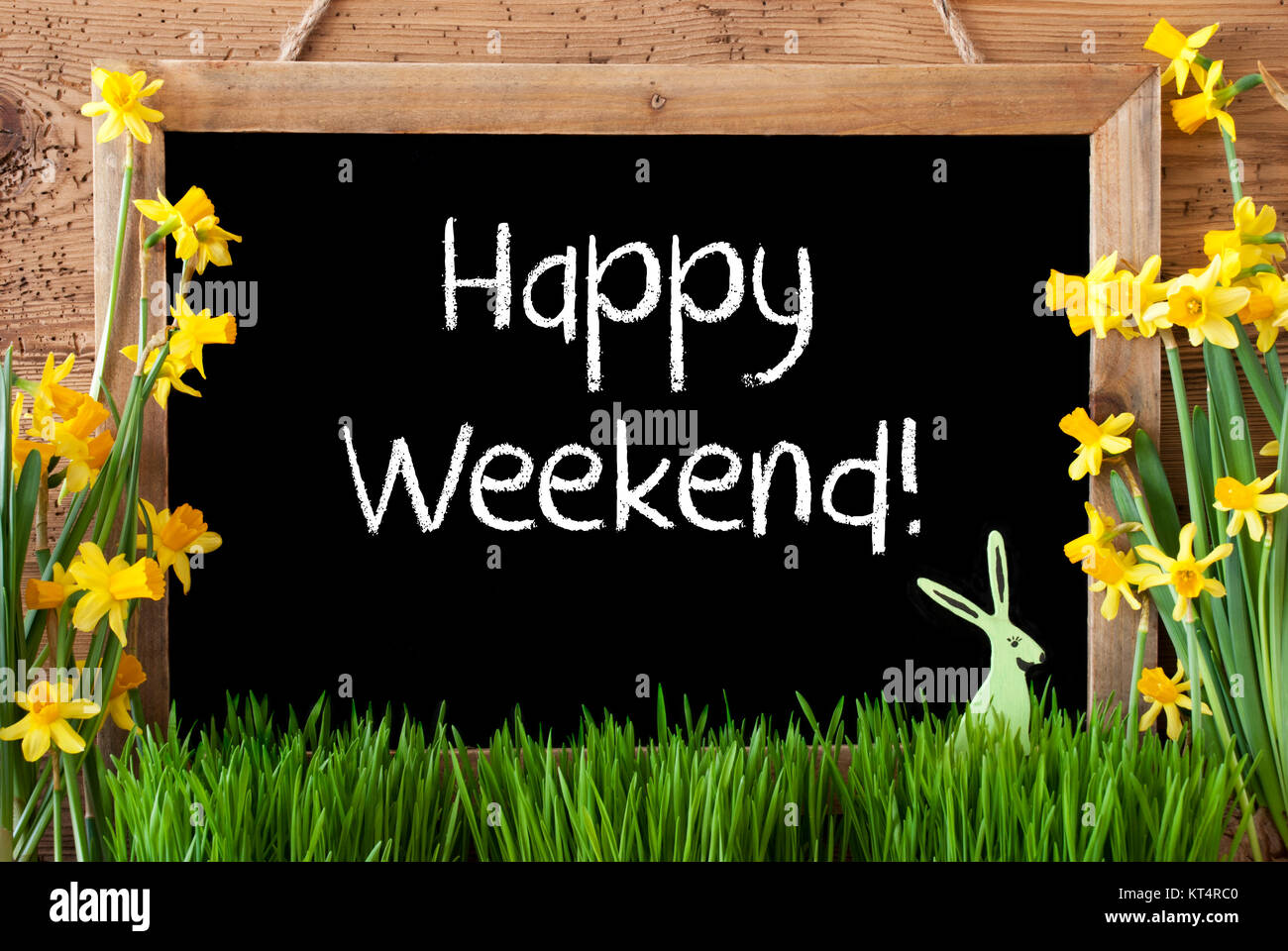 Lavagna con testo in inglese Happy Weekend. Fiori di Primavera Nacissus o Daffodil con erba e il coniglietto di Pasqua. Rustico in legno invecchiato sfondo. Foto Stock