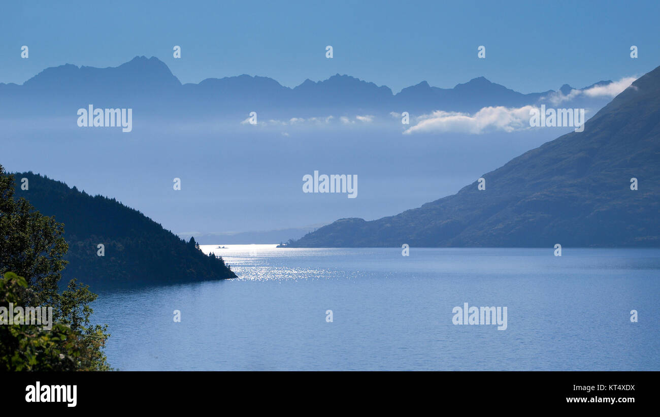 Vista della catena montuosa Remarkables sul lago Wakatipu vicino a Queenstown, Nuova Zelanda in blu la mattina presto haze Foto Stock