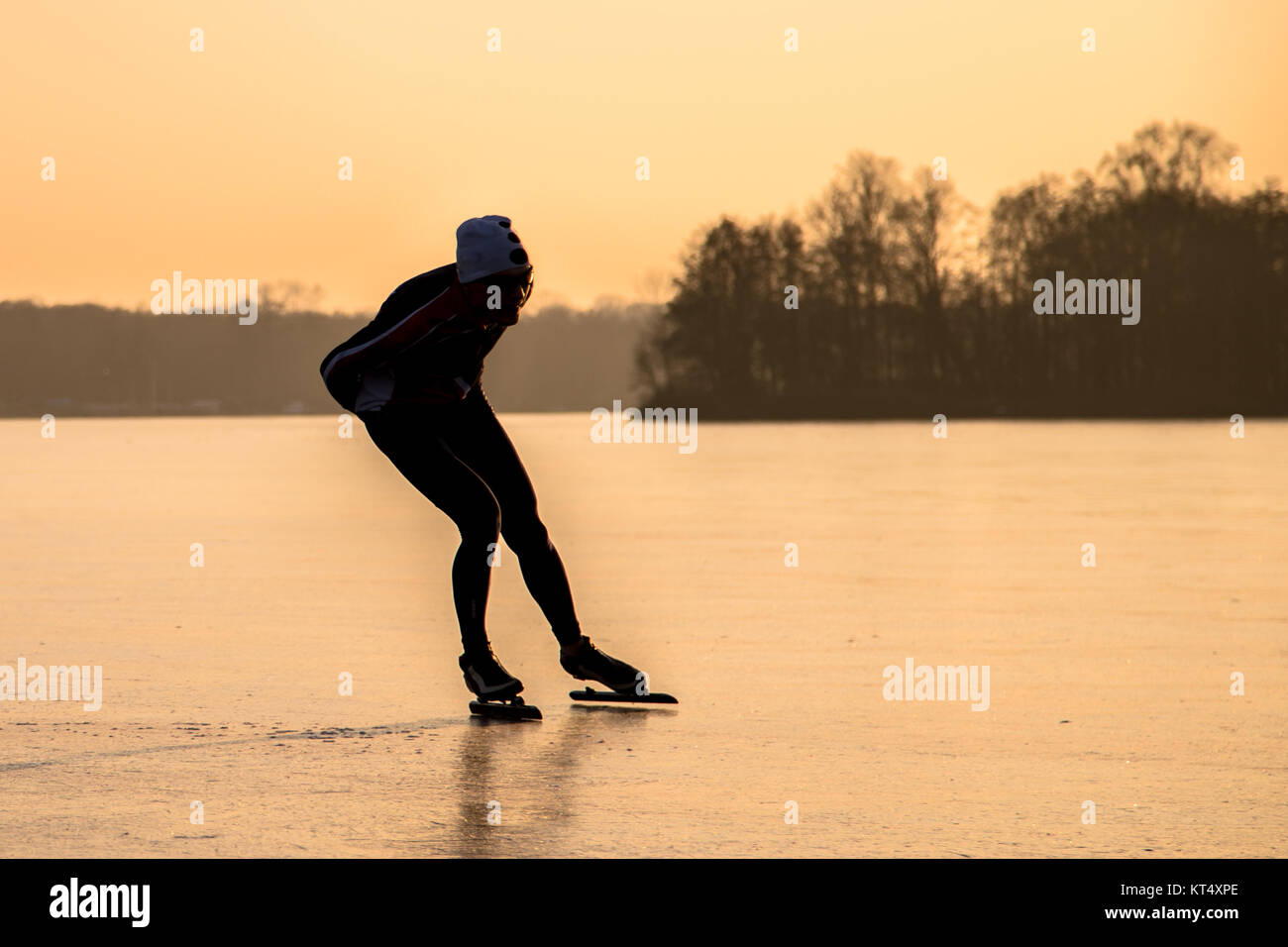 Ghiaccio pattinaggio di velocità silhouette in luce arancione del tramonto sul lago ghiacciato nei Paesi Bassi Foto Stock