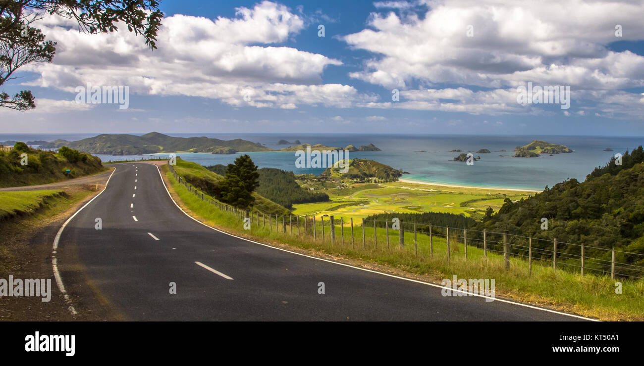 Invitante strada attraverso la Nuova Zelanda campagna con il blu del mare con le isole tropicali a Bay of Islands, Northland e Nuova Zelanda Foto Stock