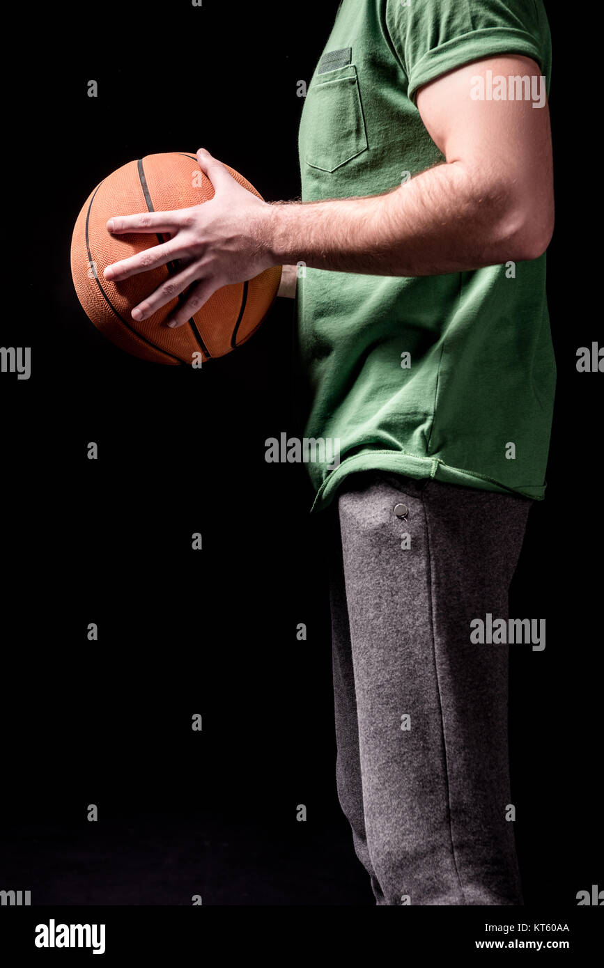 Vista laterale parziale dell'uomo holding basket ball in mani su nero Foto Stock