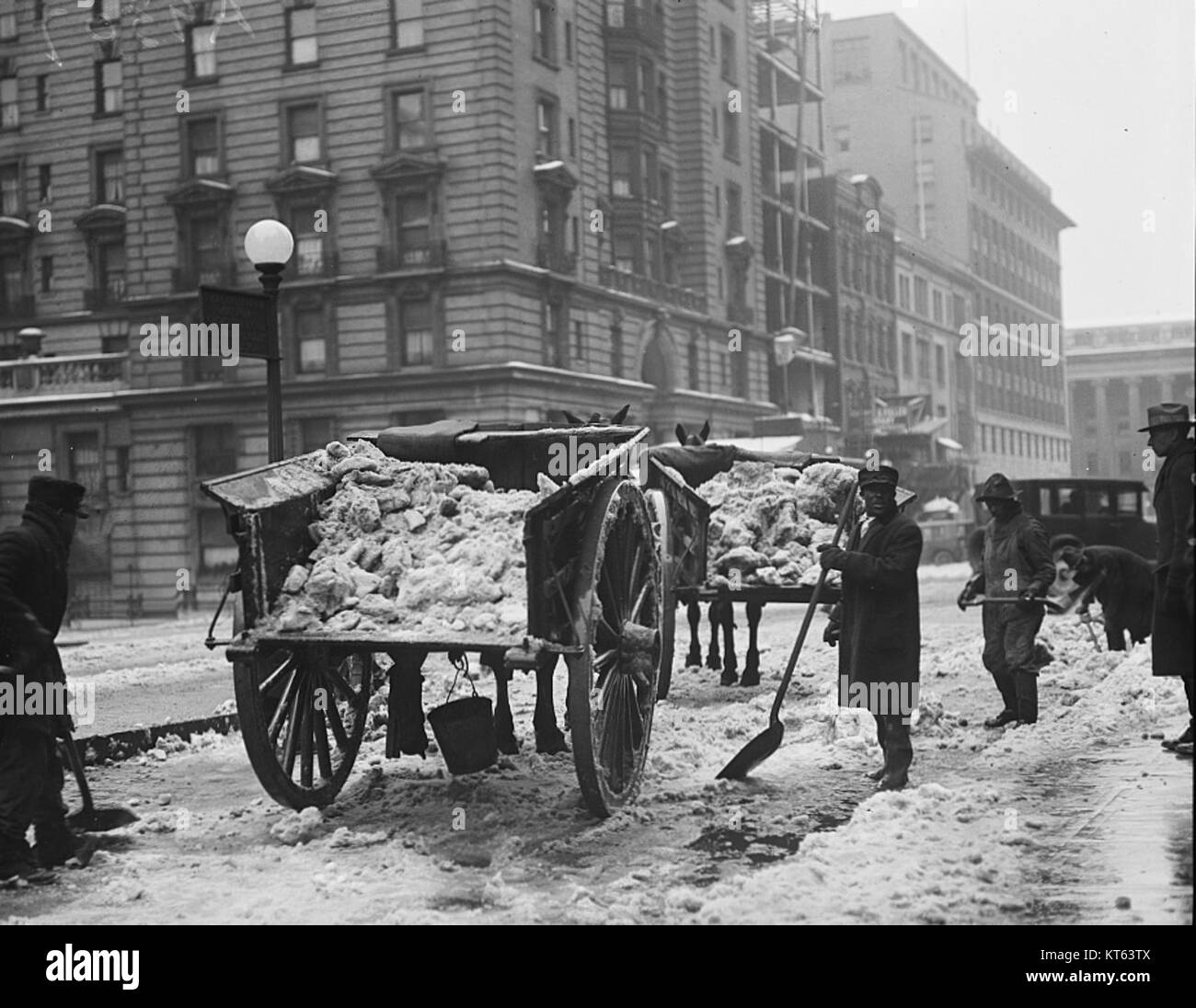 Questa fotografia cattura lo sforzo di rimozione della neve, mostrando carri pieni di neve e uomini che usano pale per pulire una strada coperta di neve, tipico del lavoro invernale nelle regioni fredde. Foto Stock