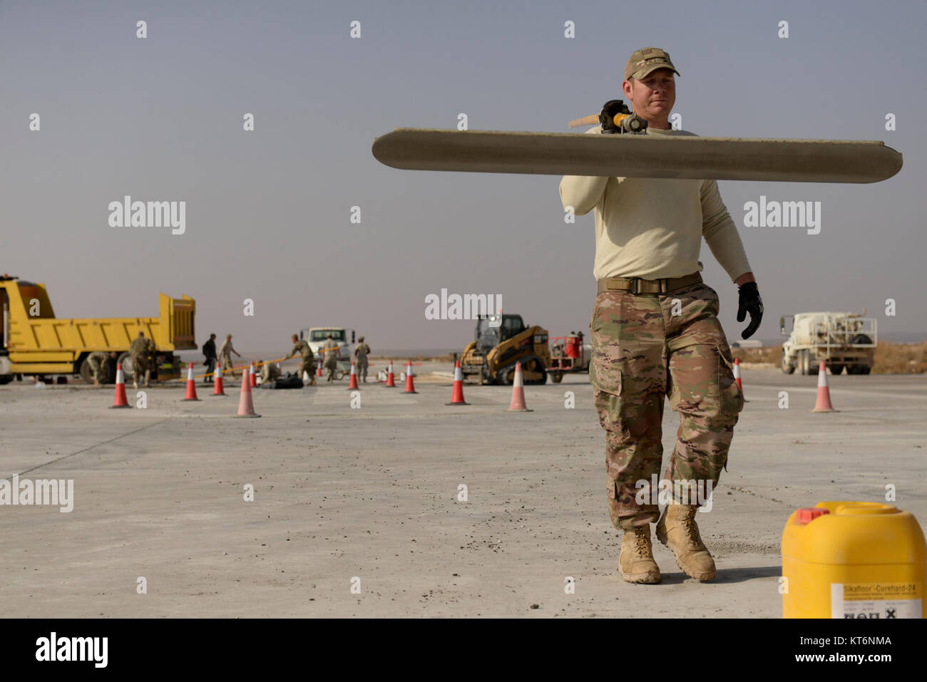 Il personale Sgt. Joshua Swertfager, nativo di Fresno, California, assegnato per la 332Expeditionary ingegnere civile Squadron porta una spatola di grandi dimensioni in un altro luogo dopo la levigatura fuori da un recente versata soletta di calcestruzzo sulla pista di una località segreta nel sud-ovest Asia nov. 28, 2017. Swertfager, una apparecchiatura pesante operatore ha lavorato con altri membri squadrone per la riparazione di una pista a causa di usura e rottura di uso costante da parte degli Stati Uniti e le forze della coalizione hanno battenti sortite contro ISIS. (U.S. Air Force Foto Stock