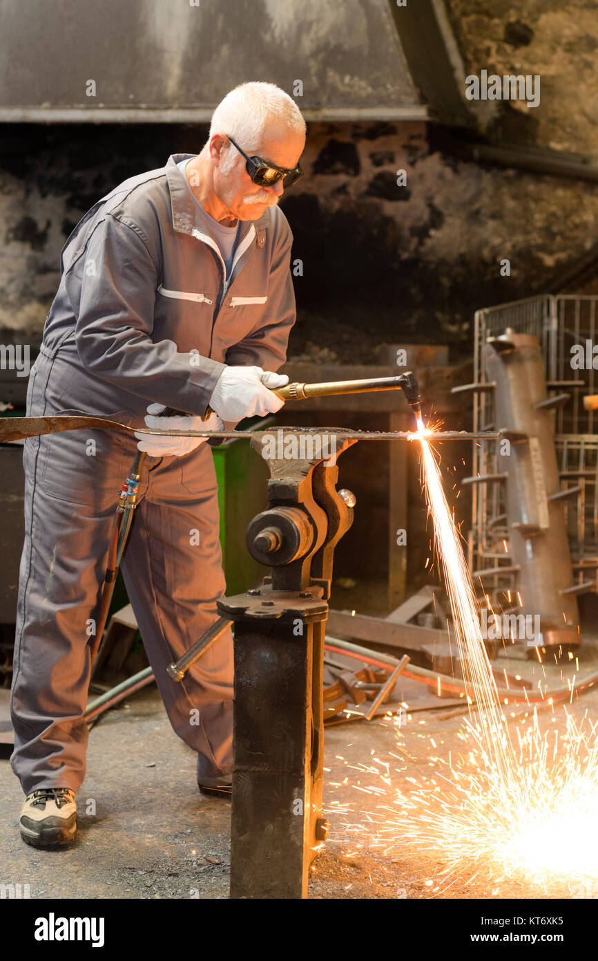 Saldatore senior di lavoro e di equipaggiamento di protezione con saldatura a scintilla Foto Stock