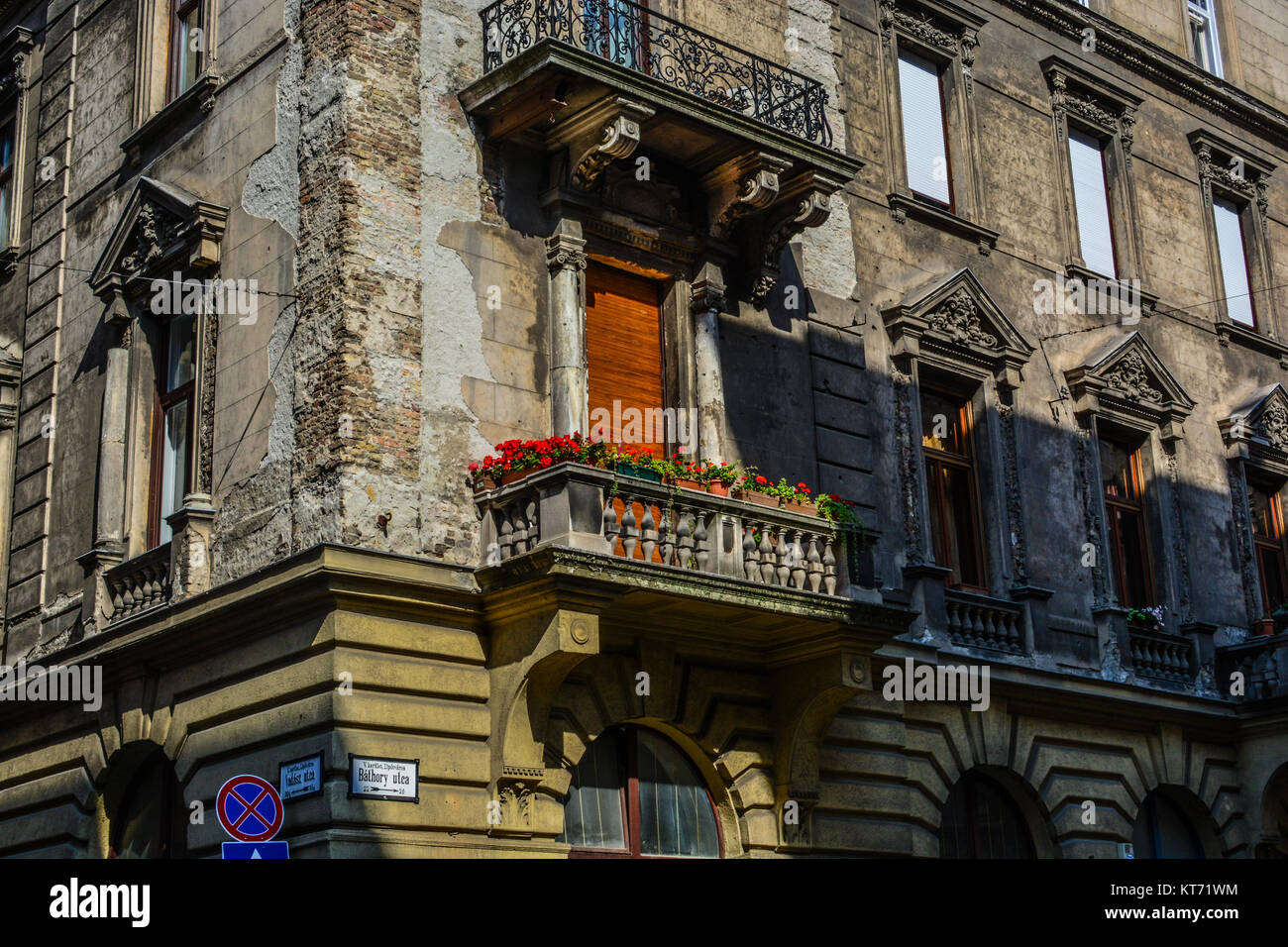 Un vecchio edificio di appartamenti in Bathory Utca in Parlamento area di Budapest Ungheria con muri cadenti e fiori di colore rosso sul balcone Foto Stock