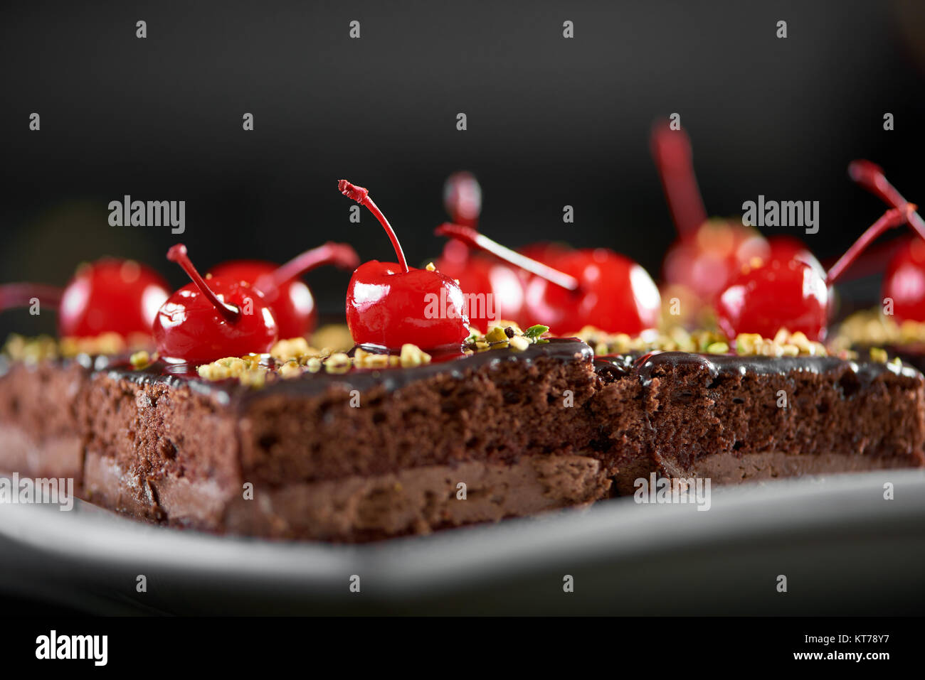 Deliziosa la pace di torta ricoperta con glassa di cioccolato e decorate con cocktail rosso ciliegia. Guarda gustosa. Sfondo scuro. Foto Stock