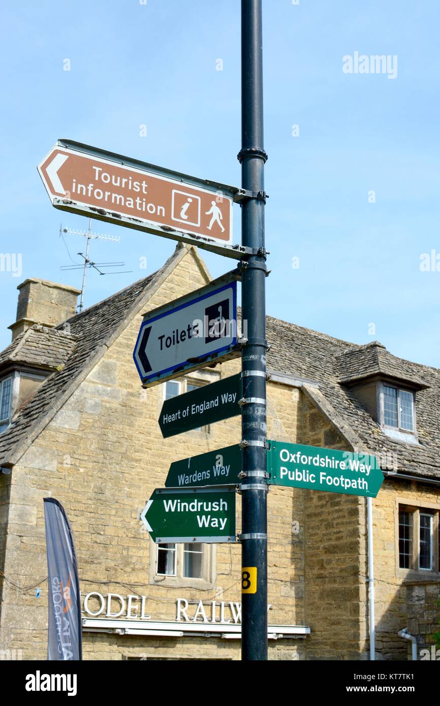 Street e segnali di informazione con edificio di pietra gialla in background, a Bourton sull'acqua, Gloucestershire, Regno Unito Foto Stock