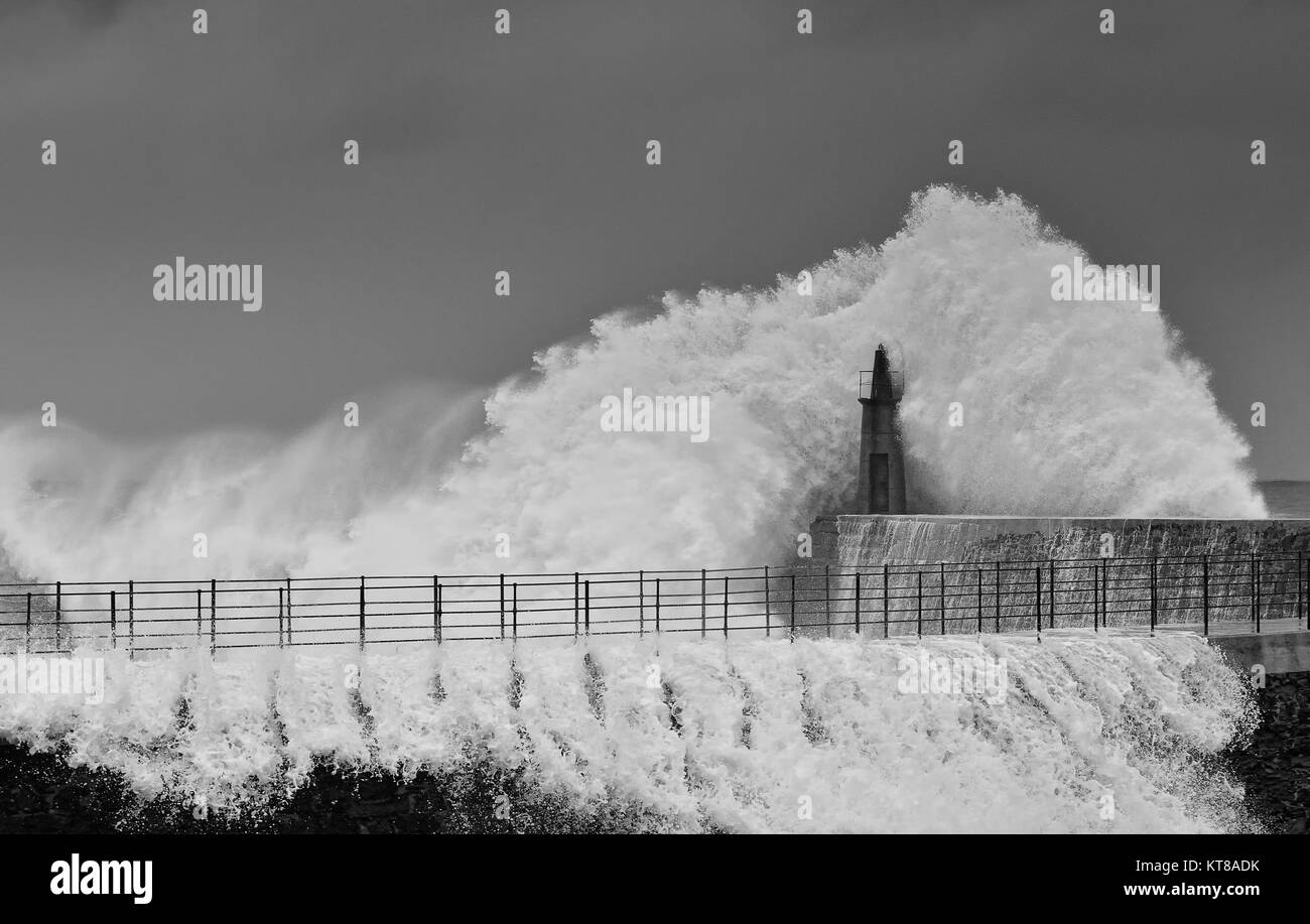 Onda di tempesta oltre il vecchio faro e il molo di Viavelez nelle Asturie, Spagna. Foto Stock