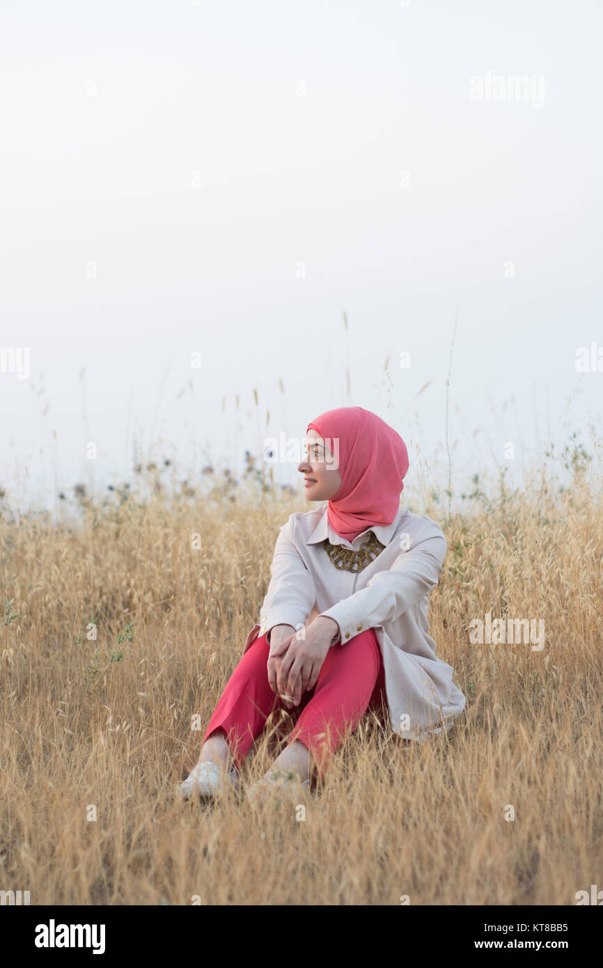 Felice mMuslim donna sat nel campo guardando lontano sorridente Foto Stock