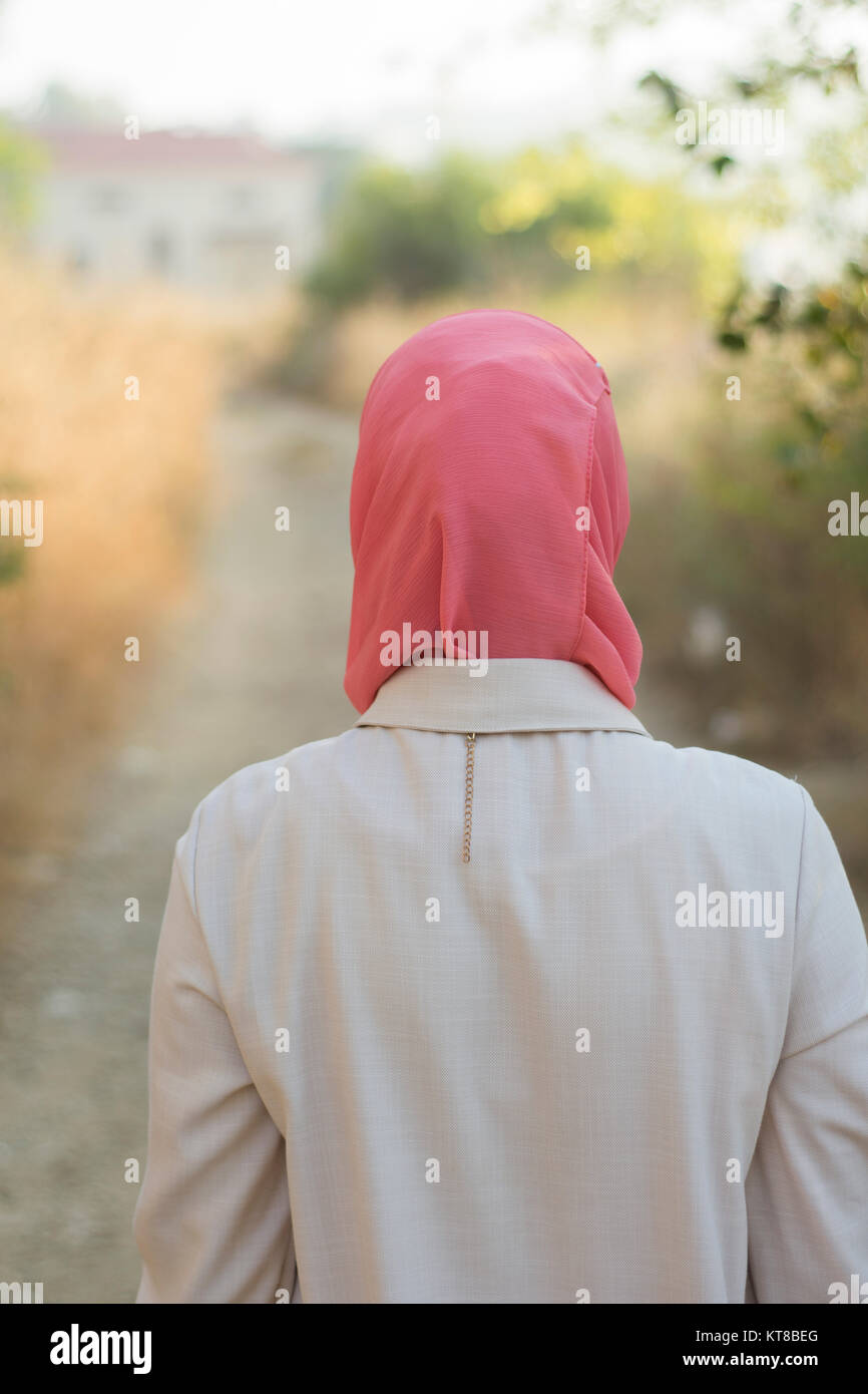 Vista posteriore di una donna musulmana wearinghijab camminare verso una casa in campagna Foto Stock