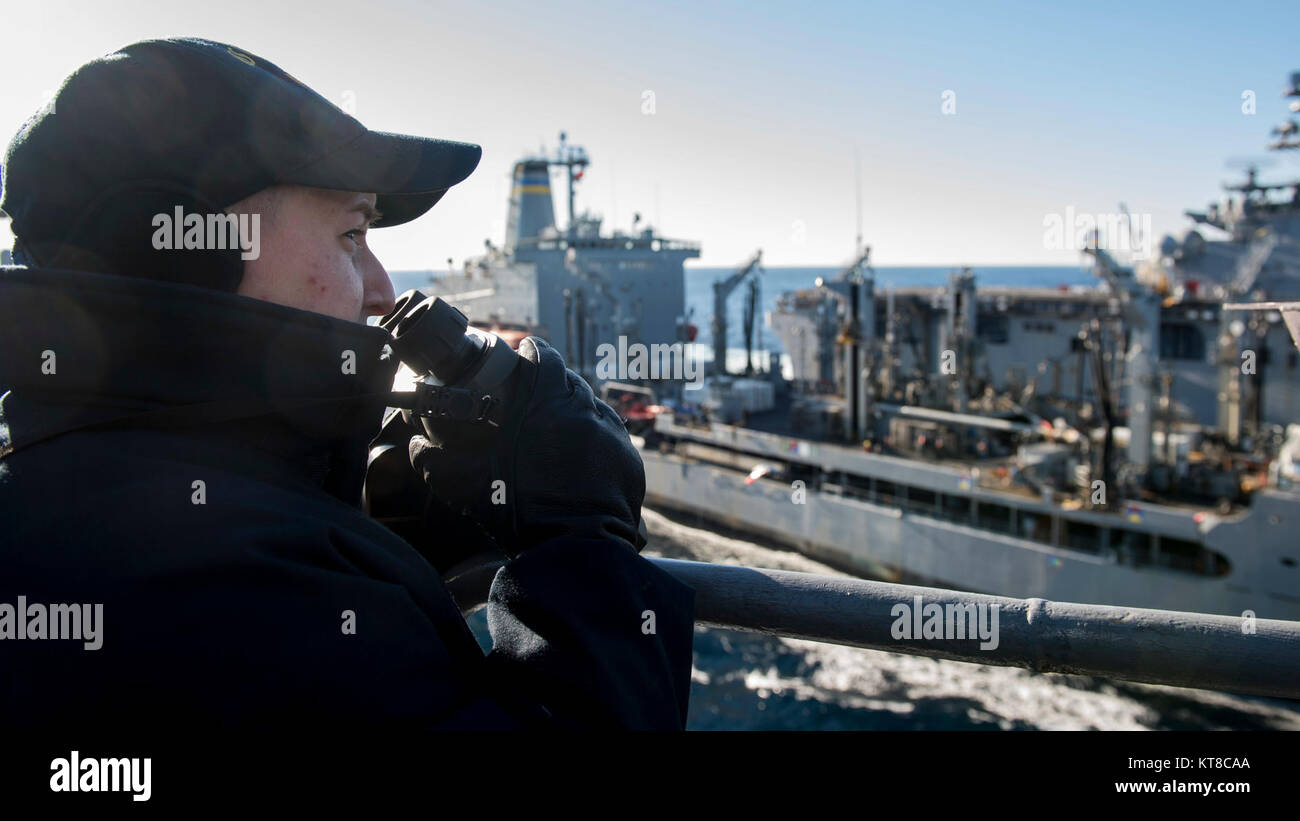 Alfiere Stephanie Fultano utilizza intervallo-trovare binocolo sulla porta laterale parafango ponte del dock landing ship USS Oak Hill (LSD 51) durante una a fianco di rifornimento collegato (CONREP) con la flotta di rifornimento USNS oliatore Big Horn (T-AO 198), centro e l'assalto anfibio nave USS Iwo Jima (LHD 7). Oak Hill recentemente completato composito combinato unità di addestramento esercizio ed è in corso la preparazione per la sua distribuzione programmata nei primi mesi del prossimo anno. (U.S. Navy Foto Stock