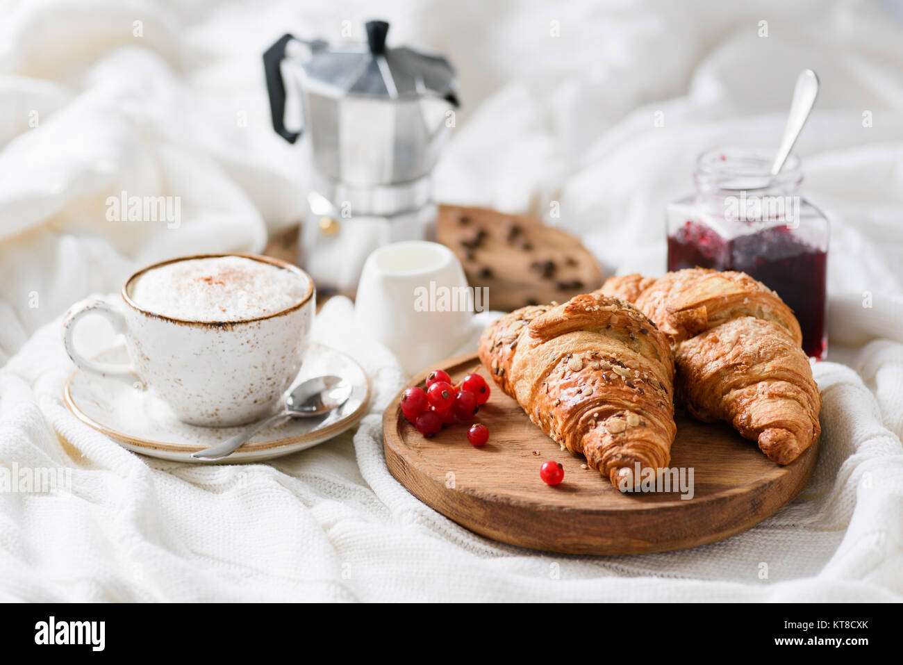 La prima colazione a letto con cornetti, marmellata, caffè cappuccino con panna e schiuma di latte. Visualizzazione orizzontale Foto Stock