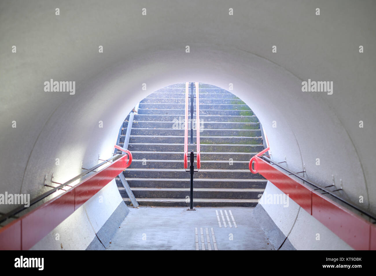 Simmetriche tunnel pedonale con un rosso corrimano in ferro e una scala alla fine Foto Stock