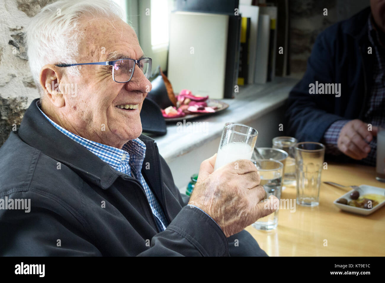 Larissa, Grecia - Ottobre 8th, 2017: un anziano uomo felice di bere Ouzo con olive (mezedes) all'interno di un tradizionale Ouzeri taverna greca. Foto Stock