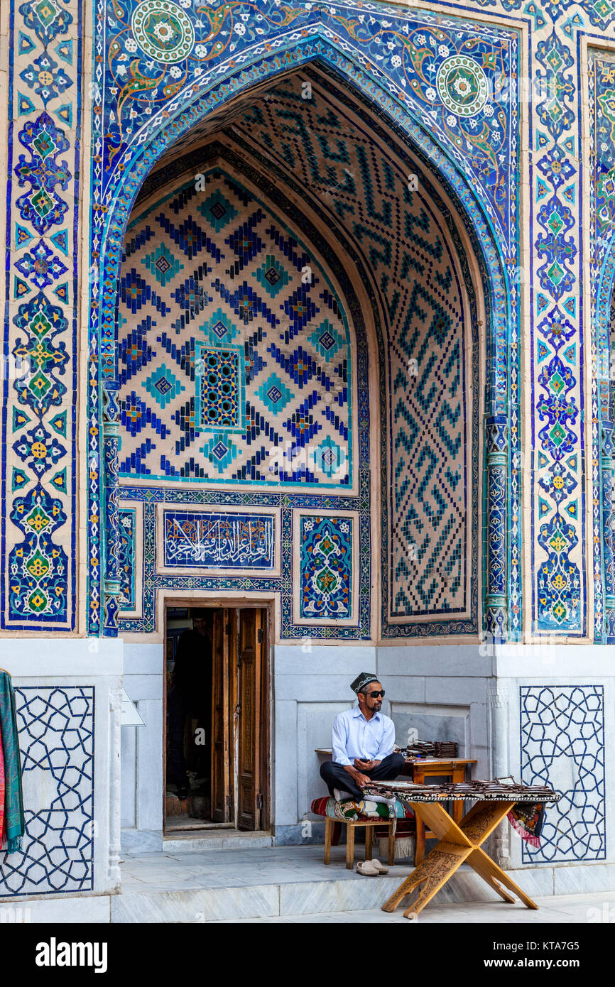 Un bottegaio seduto fuori il suo negozio all'interno del Ulugh Beg Madrassa, Il Registan, Samarcanda, Uzbekistan Foto Stock