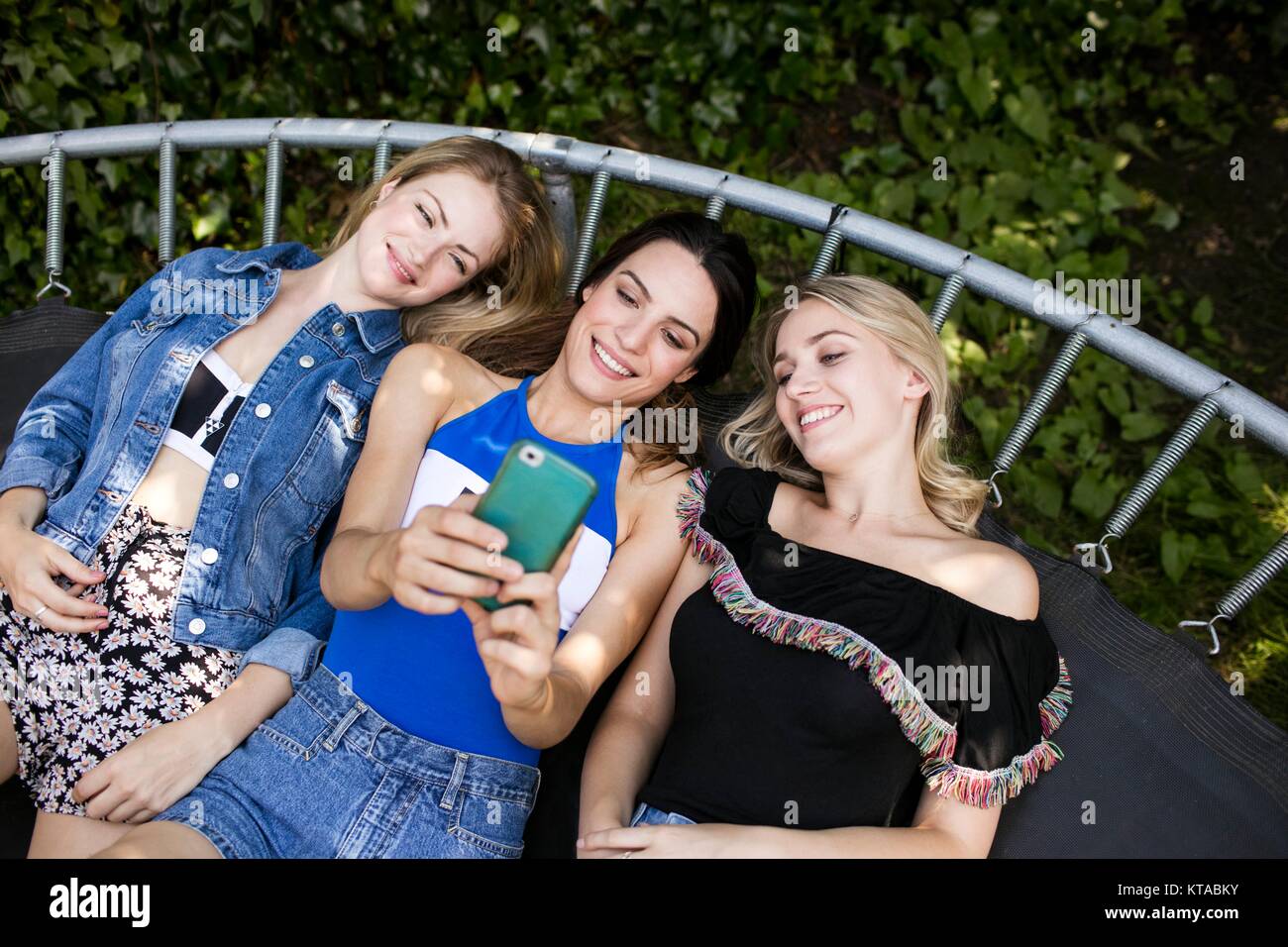 Tre giovani donne giacente sul trampolino con lo smartphone. Foto Stock