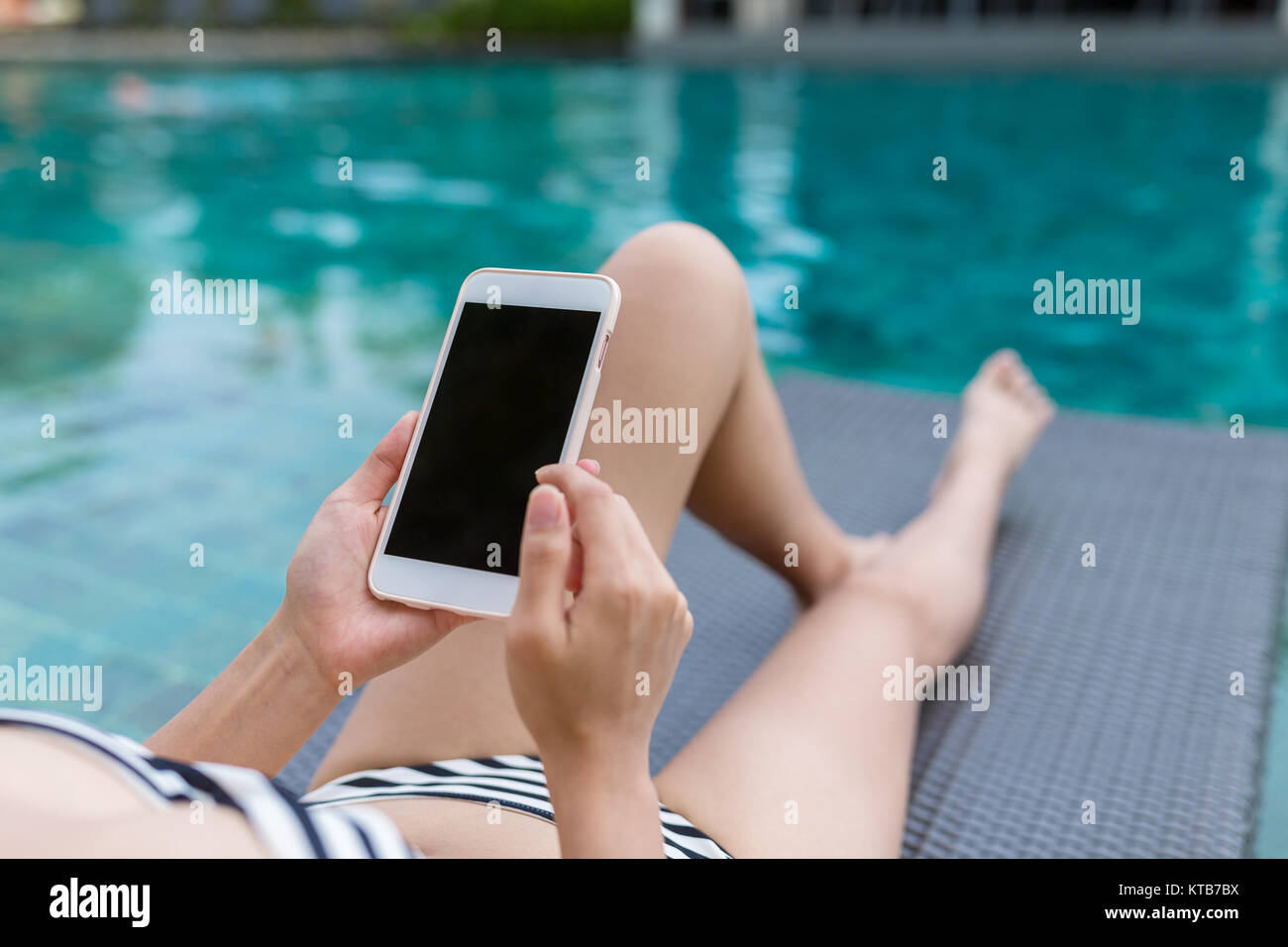 Donna godono di bagno di sole e utilizzando il telefono cellulare in piscina Foto Stock