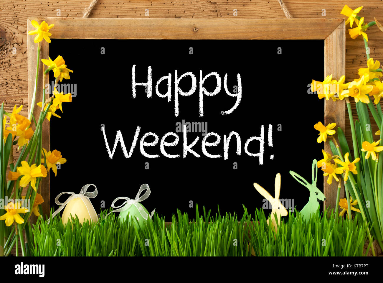 Lavagna con testo in inglese Happy Weekend. Fiori di Primavera Nacissus o Daffodil con erba, Uovo di Pasqua e Bunny. Rustico in legno invecchiato sfondo. Foto Stock