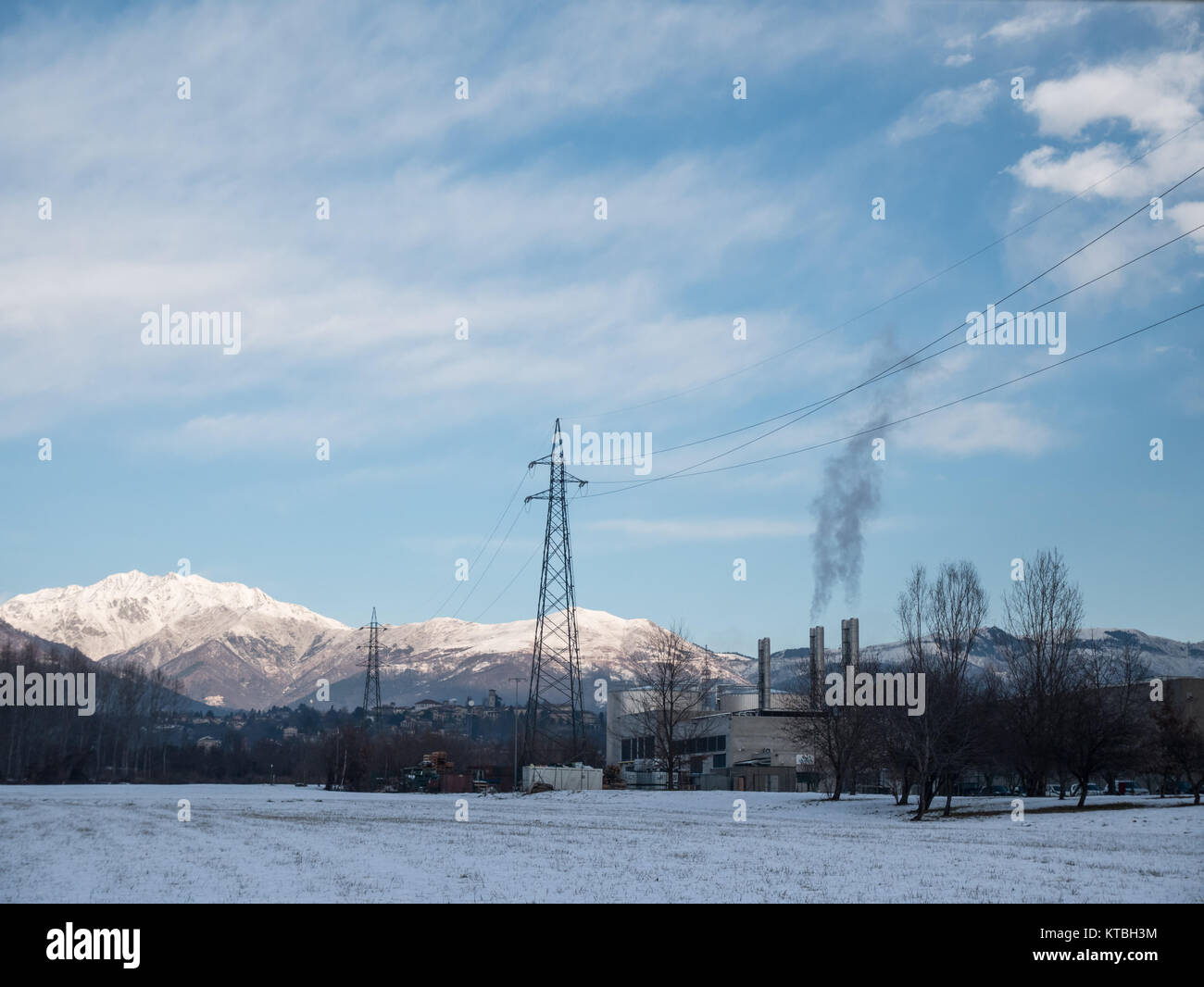 Biella, Italia - 15 dicembre 2017: Industriale paesaggio coperto di neve ai piedi delle Alpi, fabbrica con camini di fumo, nel paese di Bi Foto Stock
