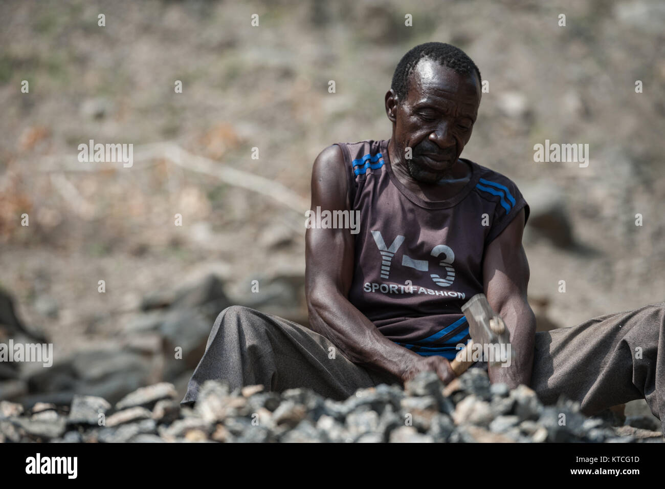 Un uomo la frantumazione di rocce nella ghiaia per il settore della costruzione in Malawi Foto Stock