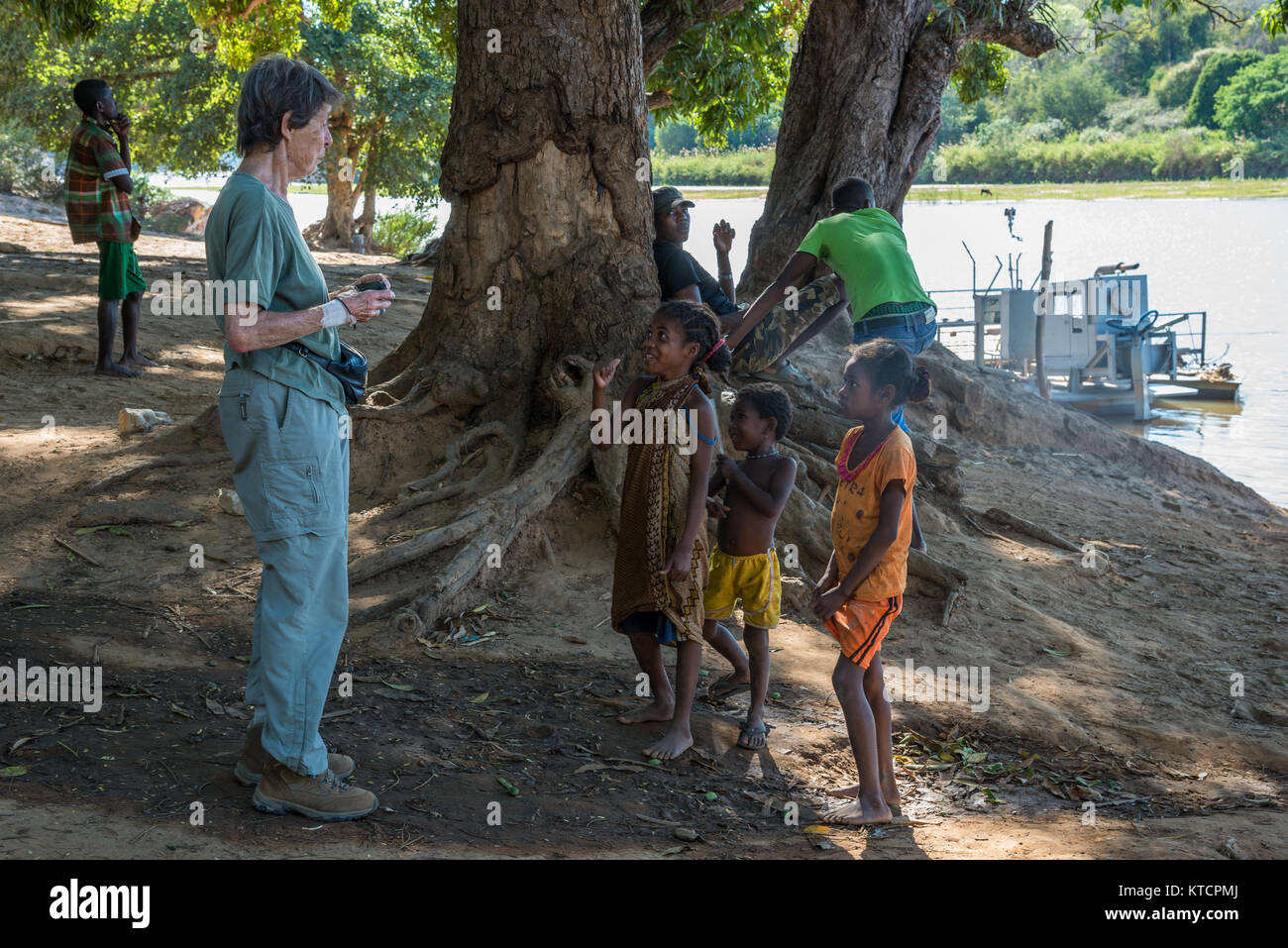 Tre giovani ragazzi malgasci curiosamente parlando ad un turista occidentale lady. Madagascar, Africa. Foto Stock