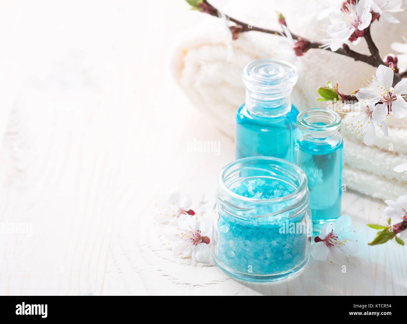 Bagno minerale sali, gel doccia, asciugamani e fiori sul tavolo di legno. DOF poco profondo. Focus sul sale. Foto Stock