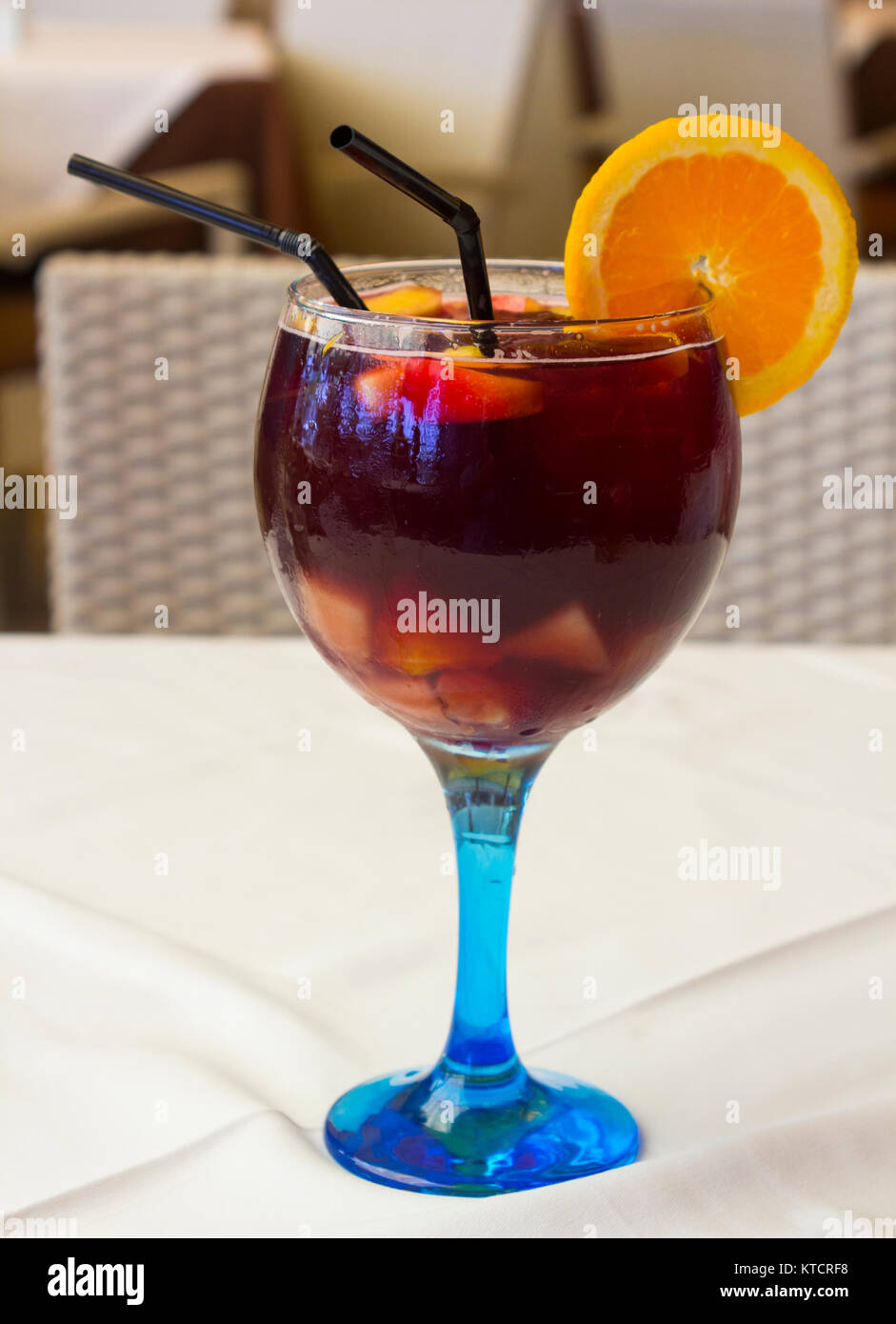 Sangria spagnola servita in un blu di gambi di bicchiere di vino con ghiaccio una fetta di arancio e due cannucce potabile Foto Stock