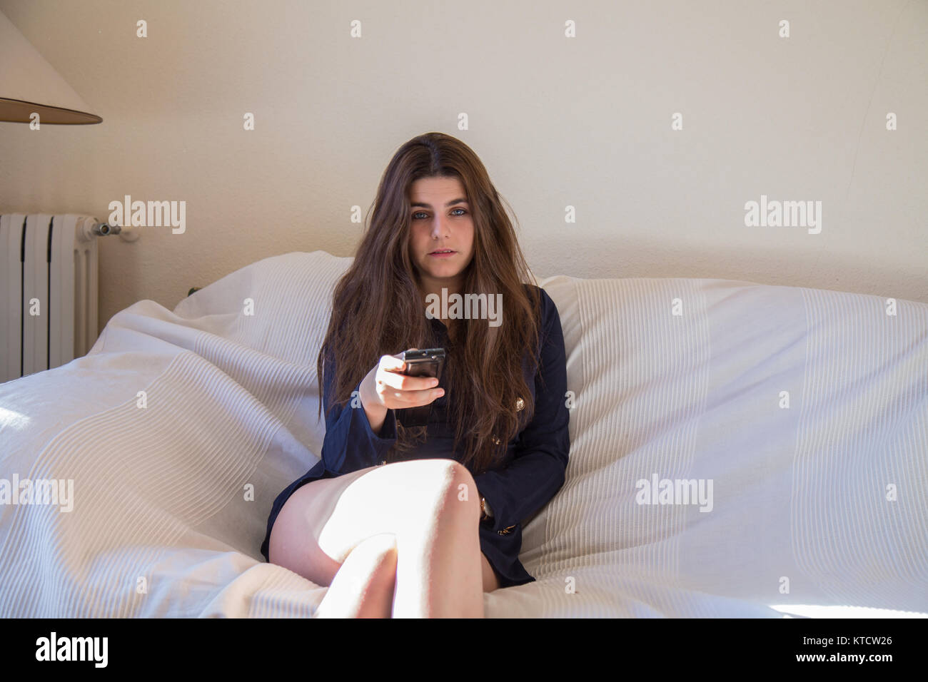 Piuttosto giovani caucasici ragazza bruna con gli occhi blu di guardare la televisione in salotto di casa sua. Ella è la commutazione dei canali. Foto Stock