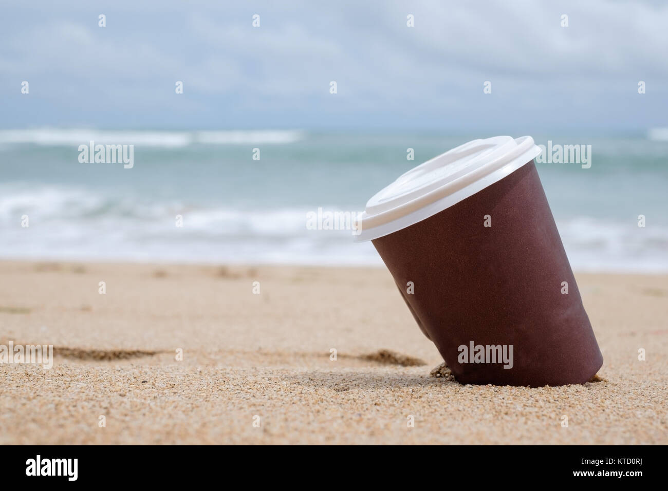 Carta marrone a tazza di caffè sulla spiaggia di sabbia di oltre il cielo nuvoloso e il mare. Hanno una deliziosa bevanda durante il riposo Foto Stock