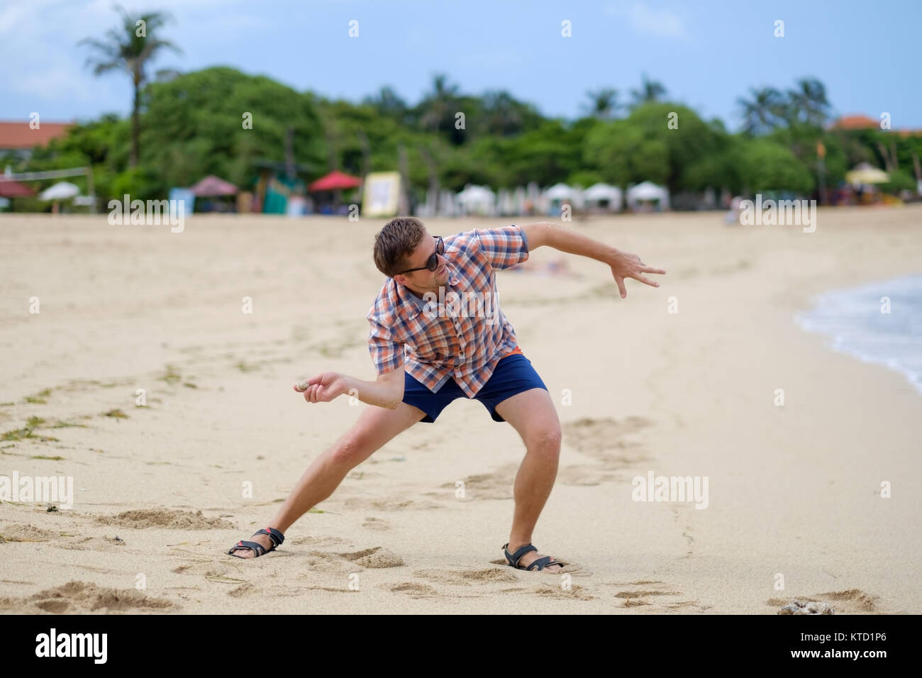 Felice uomo caucasico giocando sulla spiaggia che lanciano pietre sulla ocean, Bali Indonesia, per esterno Foto Stock