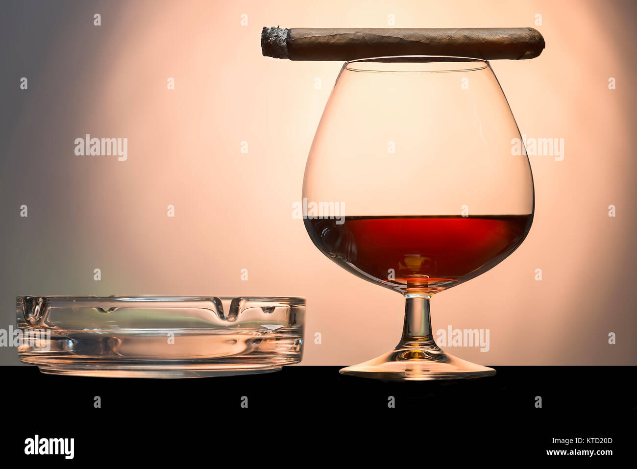 Il sigaro e il cognac con posacenere su un ripiano nero sfocatura dello sfondo arancione in mezzo Foto Stock