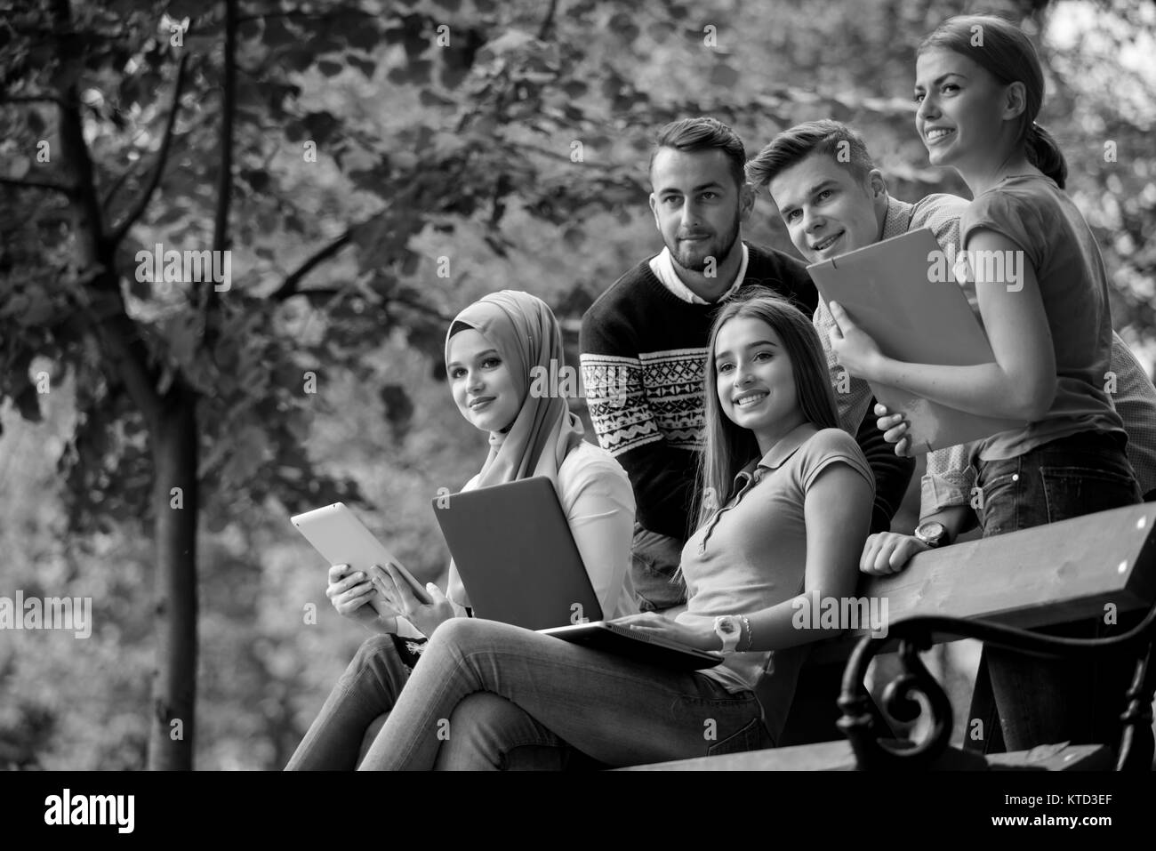 Un gruppo di giovani con laptop e tablet su una panchina nel parco, divertendosi, parlando, appendere fuori Foto Stock